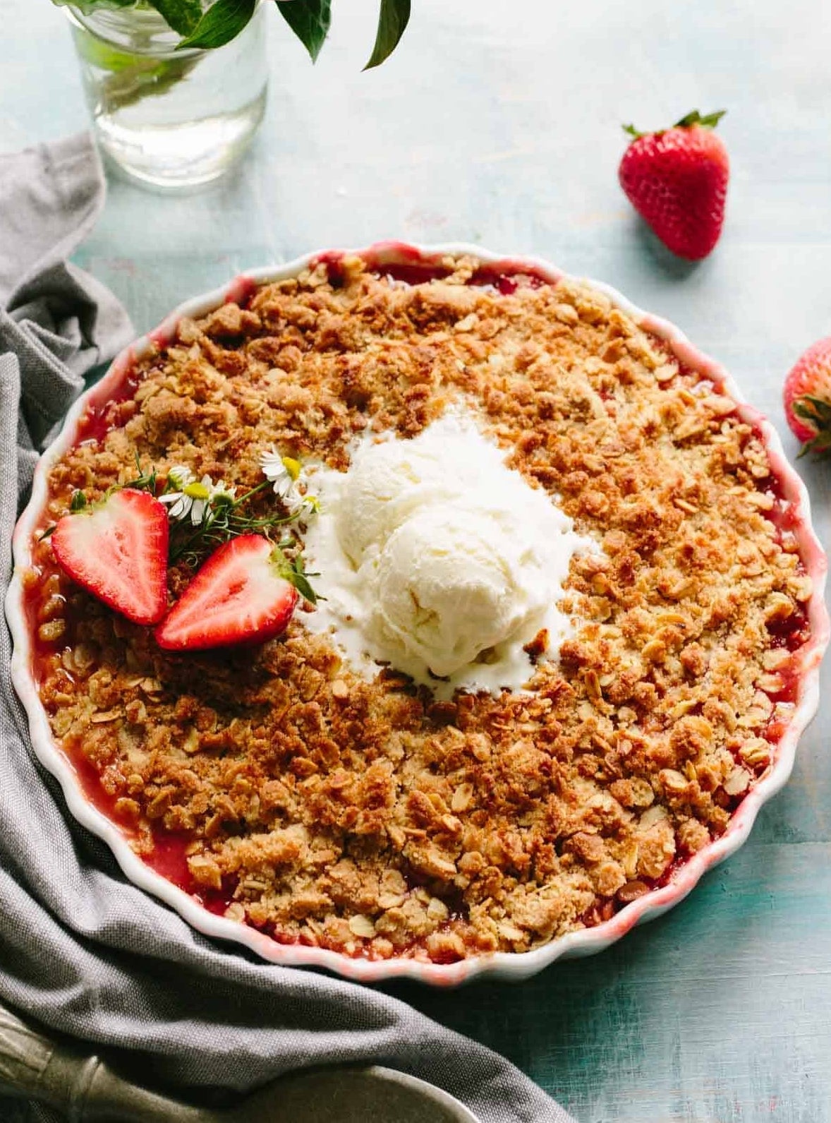 Strawberry crumble pie topped with vanilla ice cream and sliced strawberries, placed beside a gray napkin on a rustic table setting