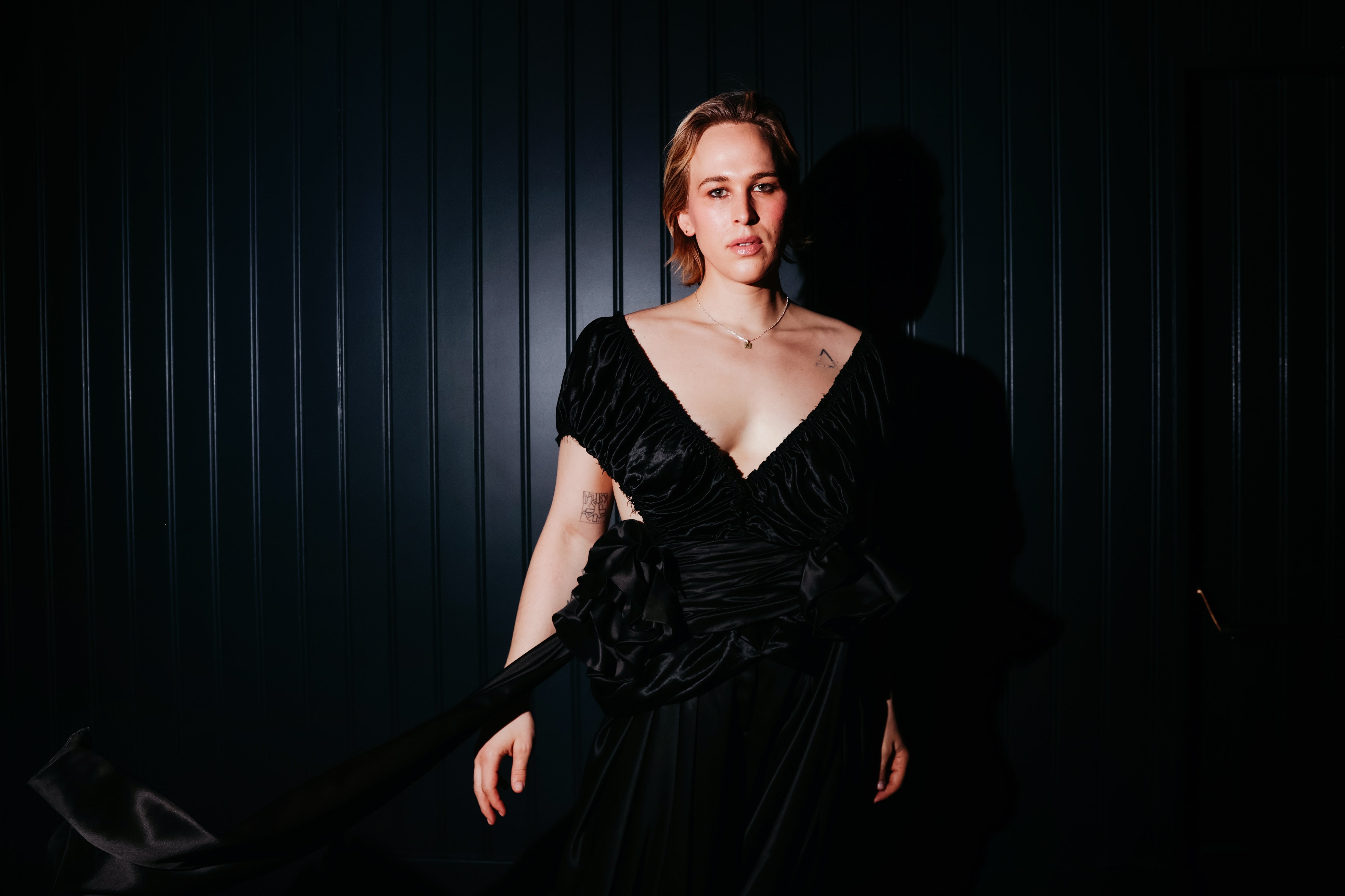 Tommy Dorfman successful  an elegant, off-the-shoulder gown poses against a acheronian  background
