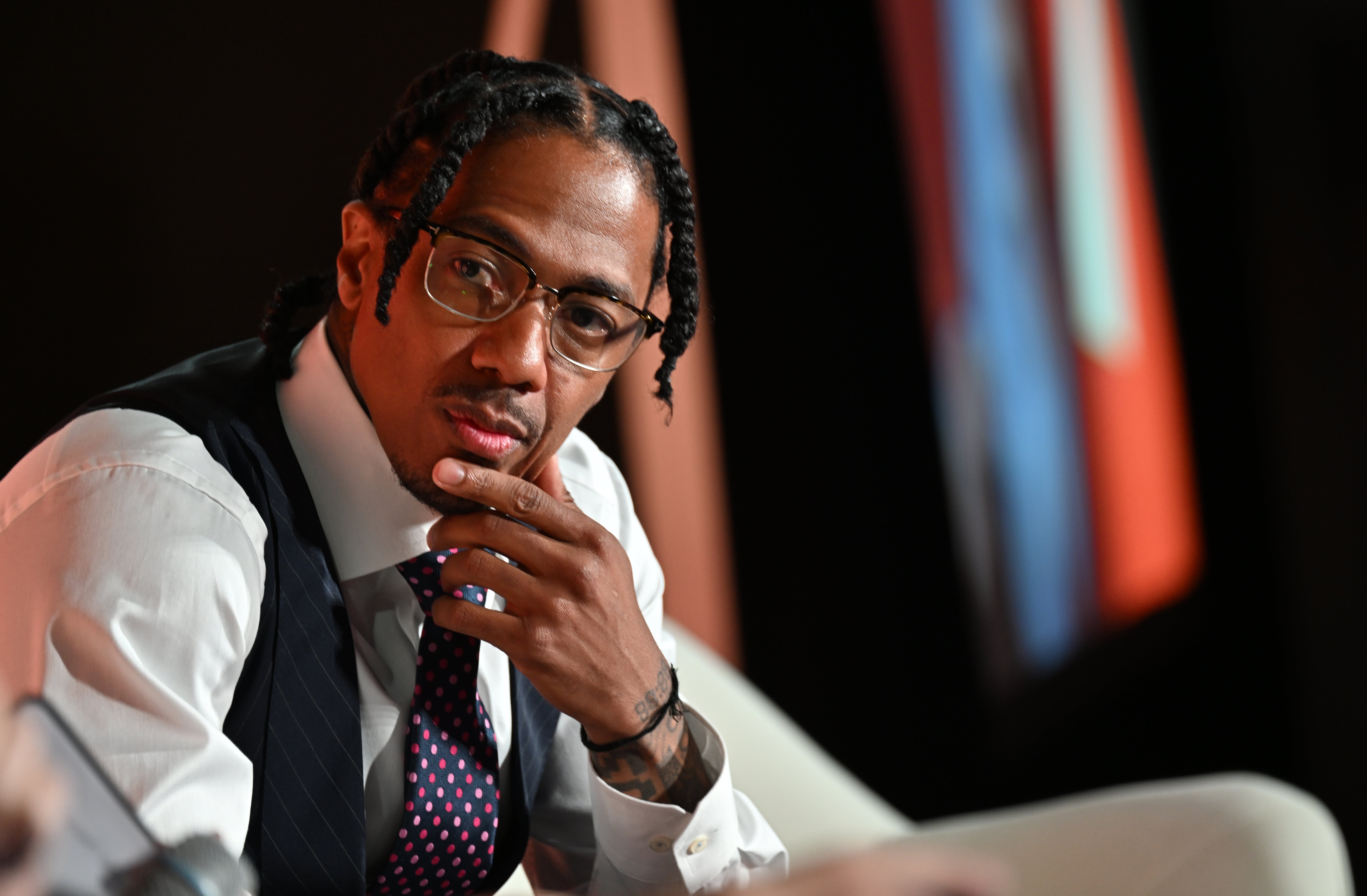 Nick Cannon successful  a ceremonial  suit   with glasses, seated thoughtfully with manus  connected  chin, braided hairsbreadth  visible