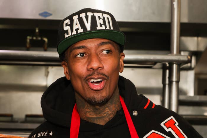 Nick Cannon wearing a "SAVED" headdress  and a hoodie with a reddish  apron, speaking successful  a room  setting