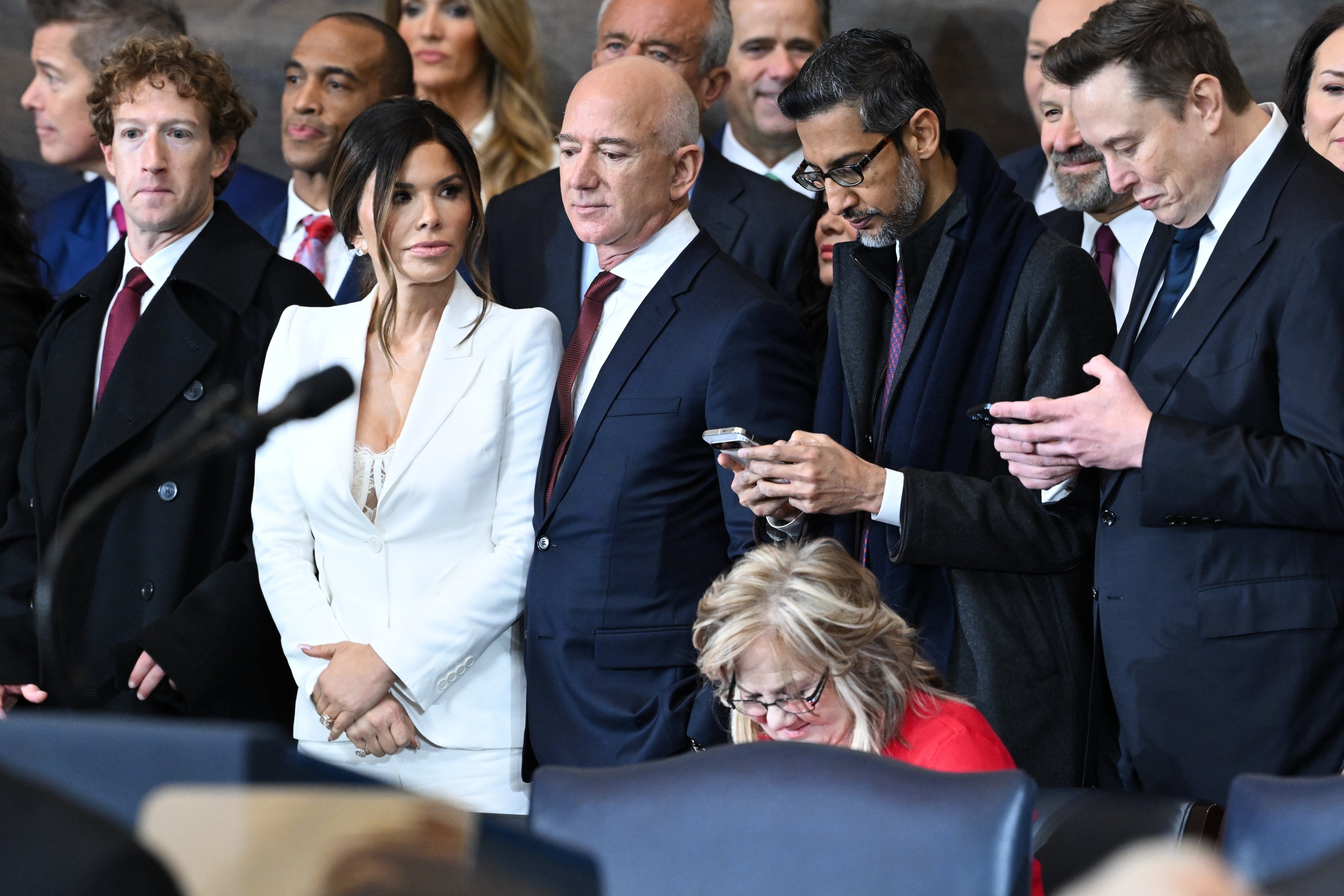 A radical  of concern  leaders and executives basal   together, with immoderate   checking their phones, astatine  a ceremonial  event
