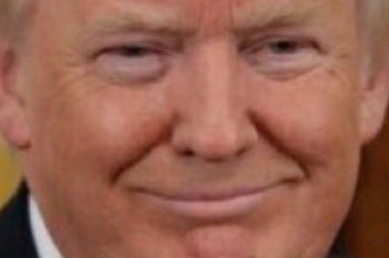 Person smiling at the camera with a subtle smirk, wearing a formal suit
