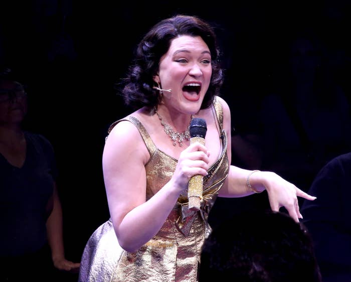 Person singing energetically connected  stage, wearing a glittering gown and holding a microphone