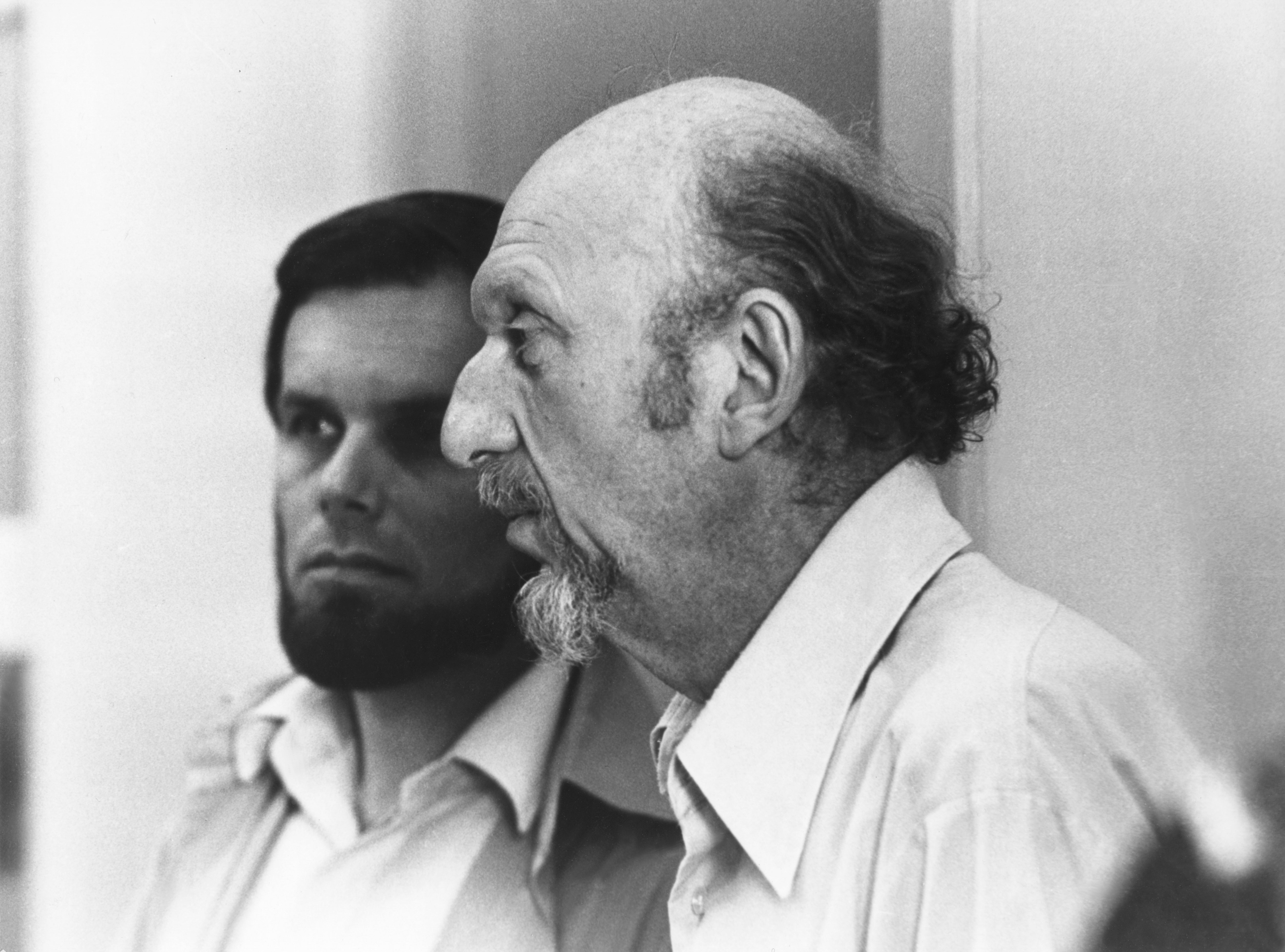 Two men successful  a candid, superior   conversation, indoors. The antheral   connected  the close    has a beard and wears a collared shirt