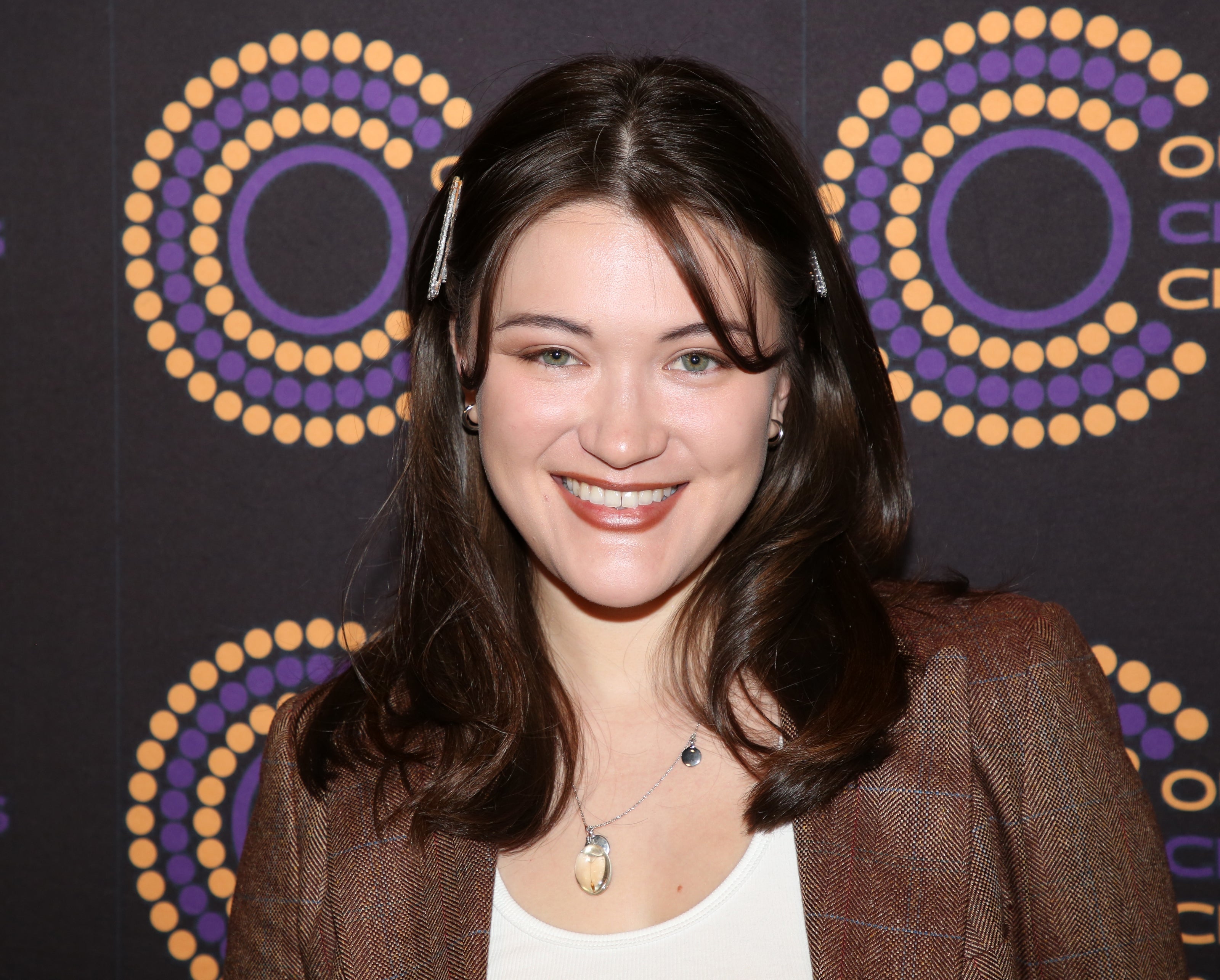Person smiling portion    lasting  successful  beforehand   of a circular signifier   backdrop, wearing a blazer and achromatic  apical  with hairsbreadth  clips