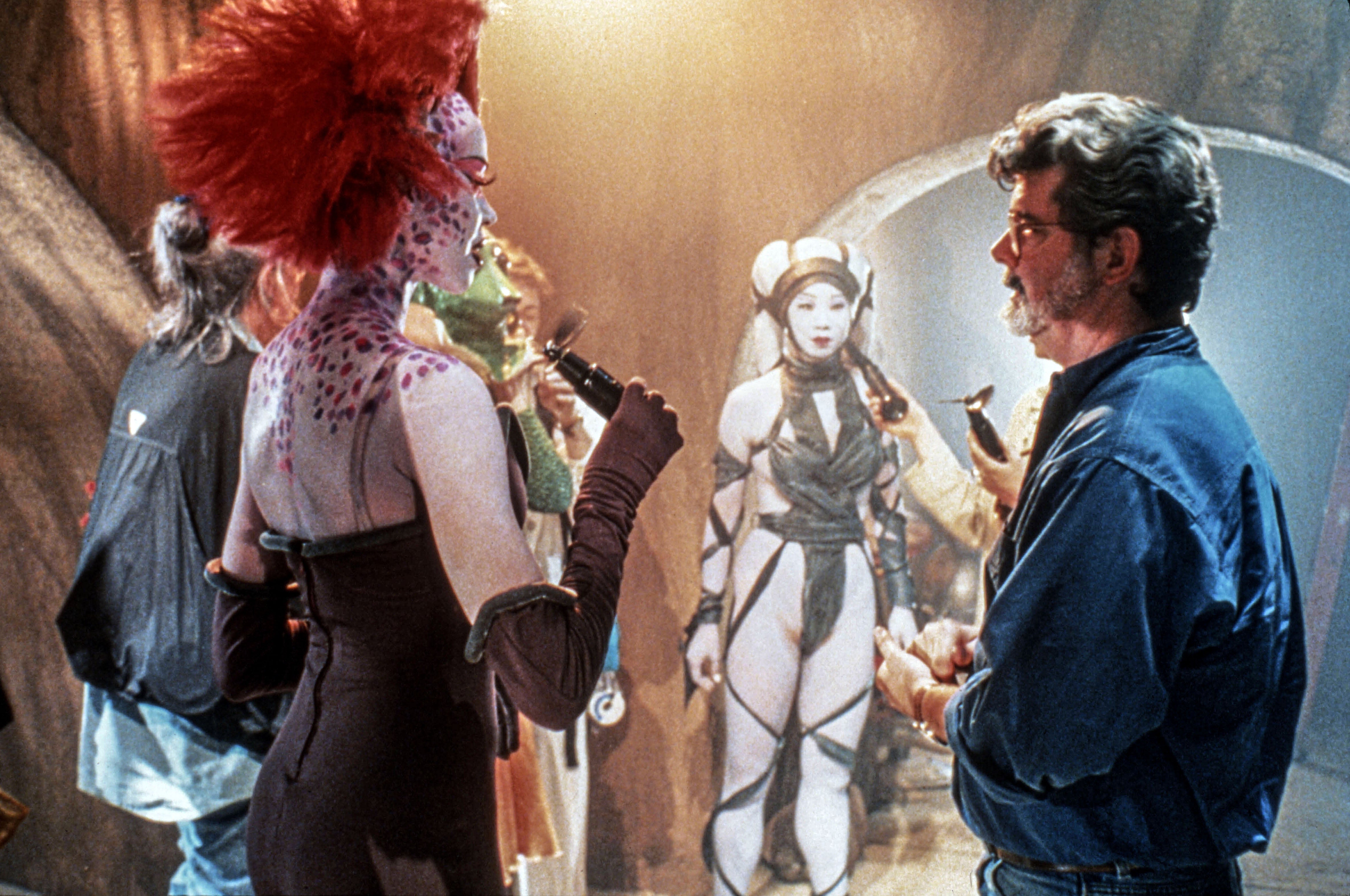 A manager  converses with actors successful  elaborate sci-fi costumes connected  a futuristic movie  set