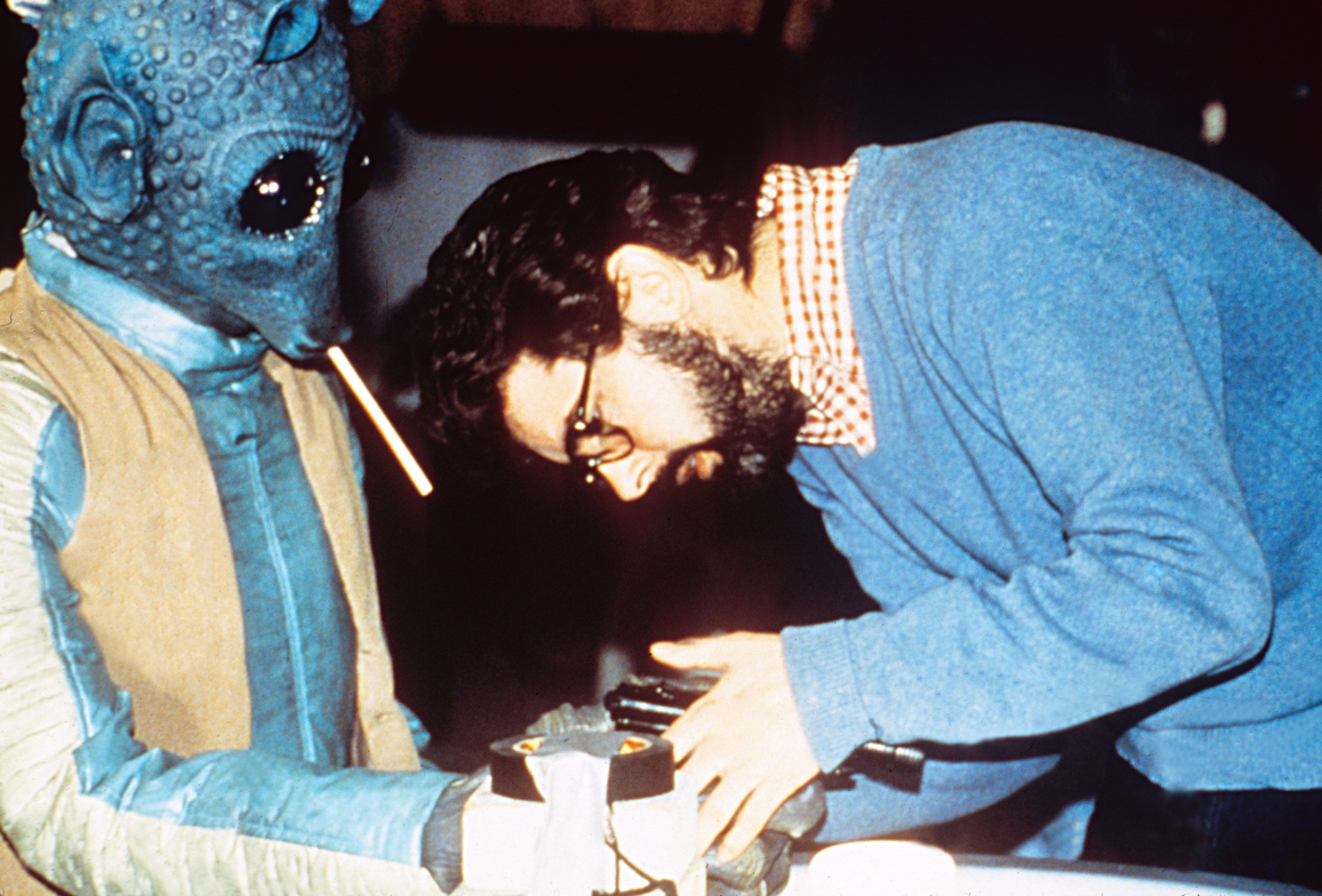 A manager  discusses a country   with an alien quality  connected  a movie  set. The alien has ample  eyes and a bladed  snout