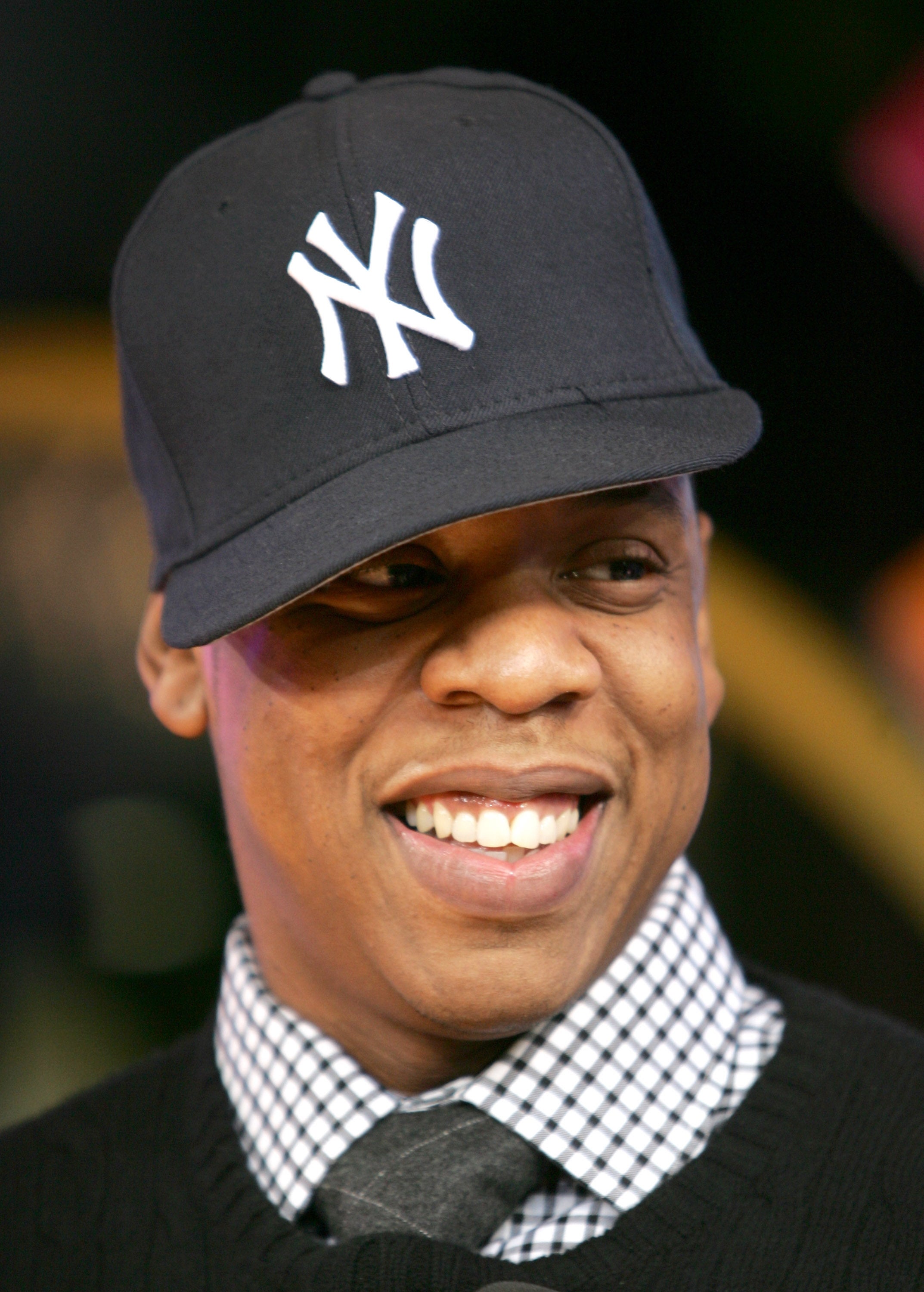 Man successful checkered shirt, sweater, and NY cap, smiling. Image relates to a question article