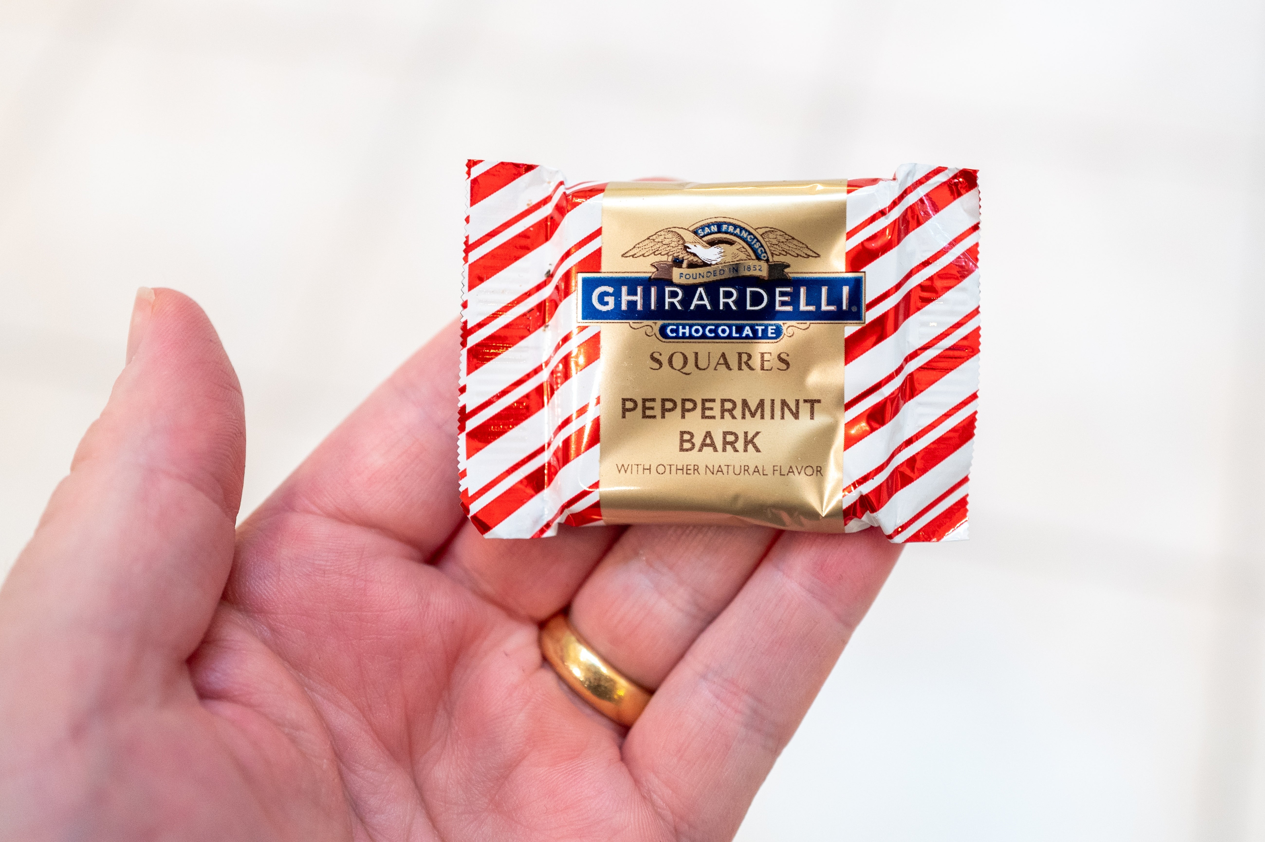 A manus holds a wrapped Ghirardelli peppermint bark cocoa square