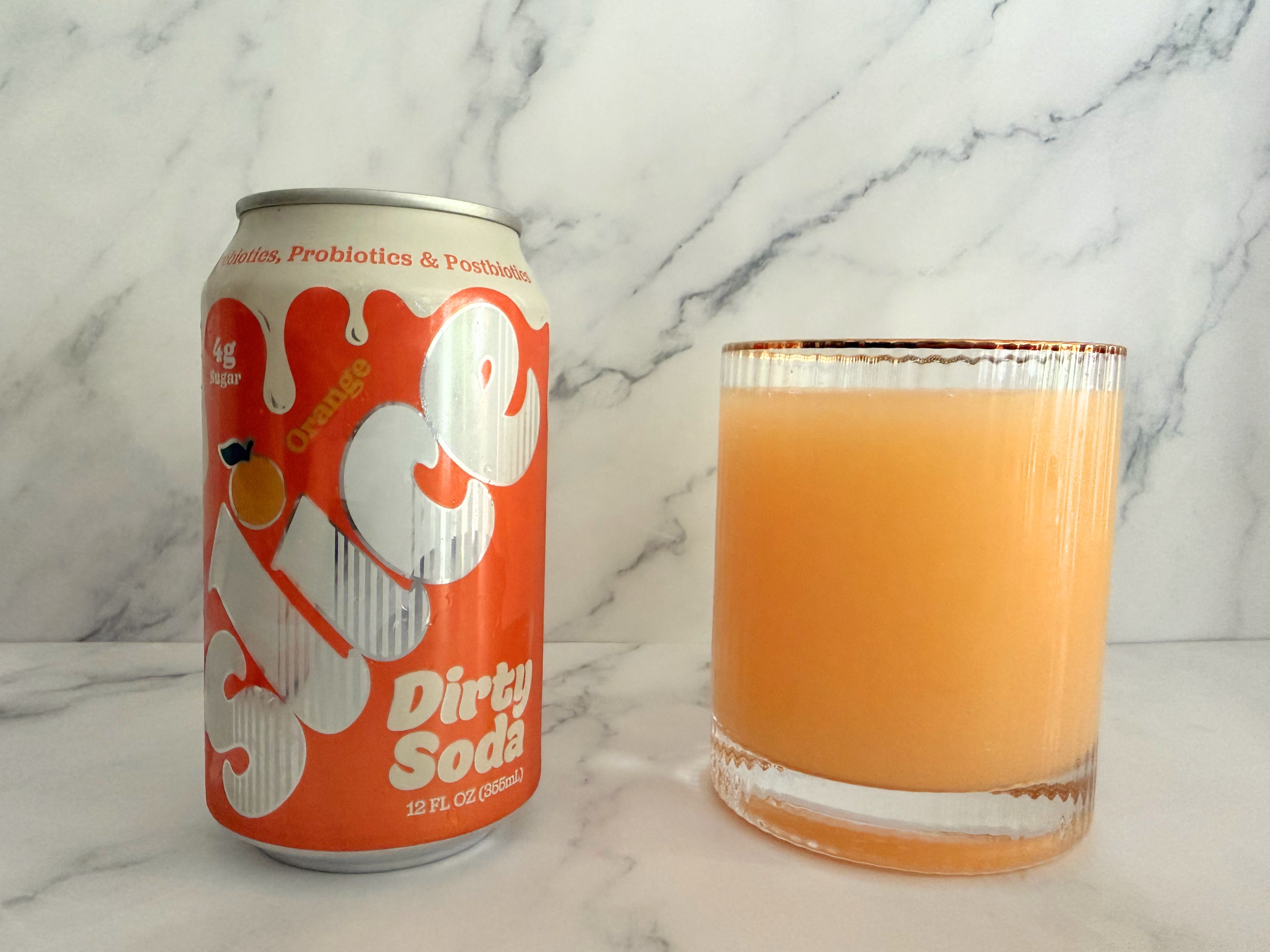 Can of orange Slice dirty soda and a glass filled with orange dirty soda on a marble surface