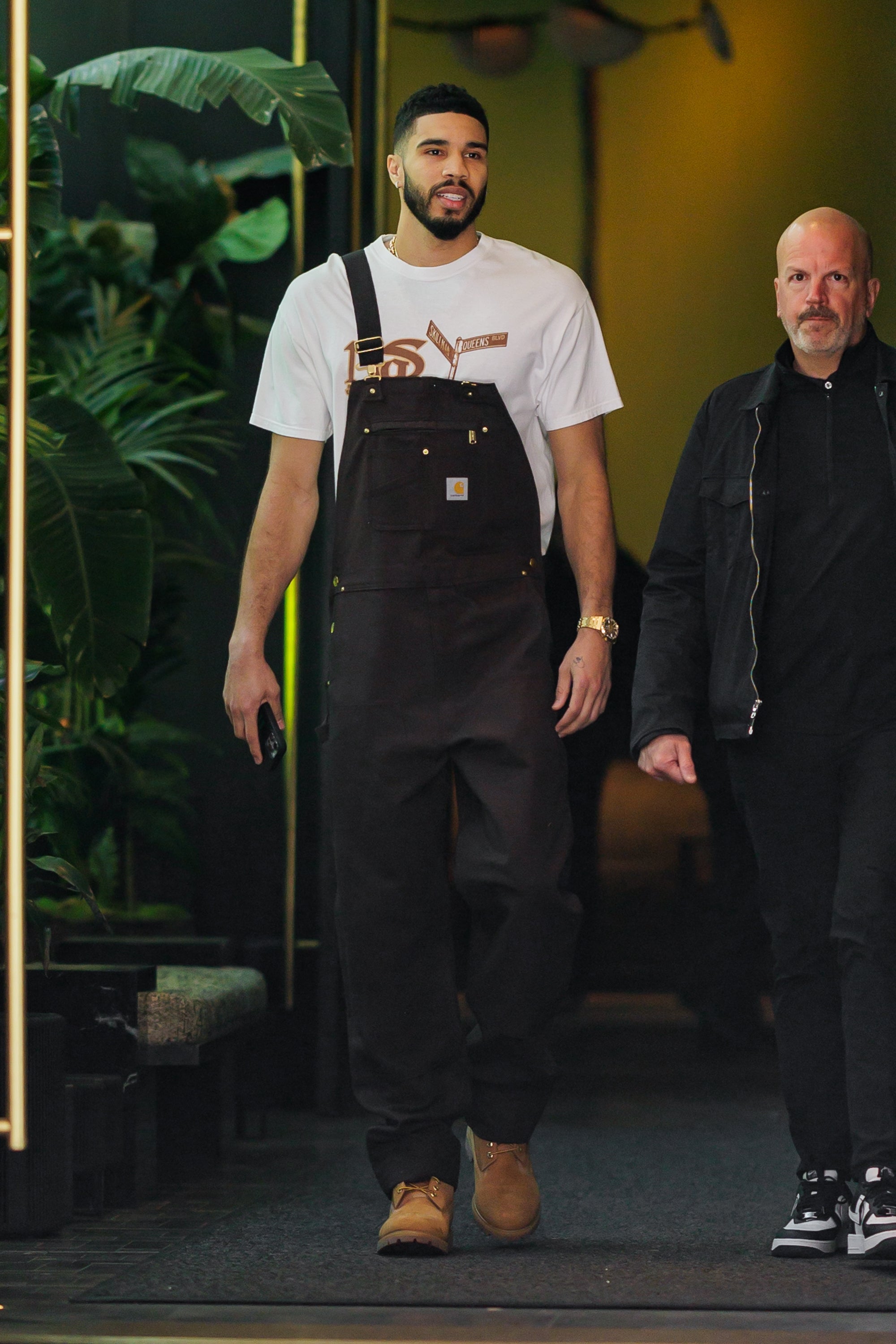 A antheral successful casual overalls and a t-shirt walks beside different person, some appearing relaxed; lush plants are visible, suggesting a question oregon leisure setting