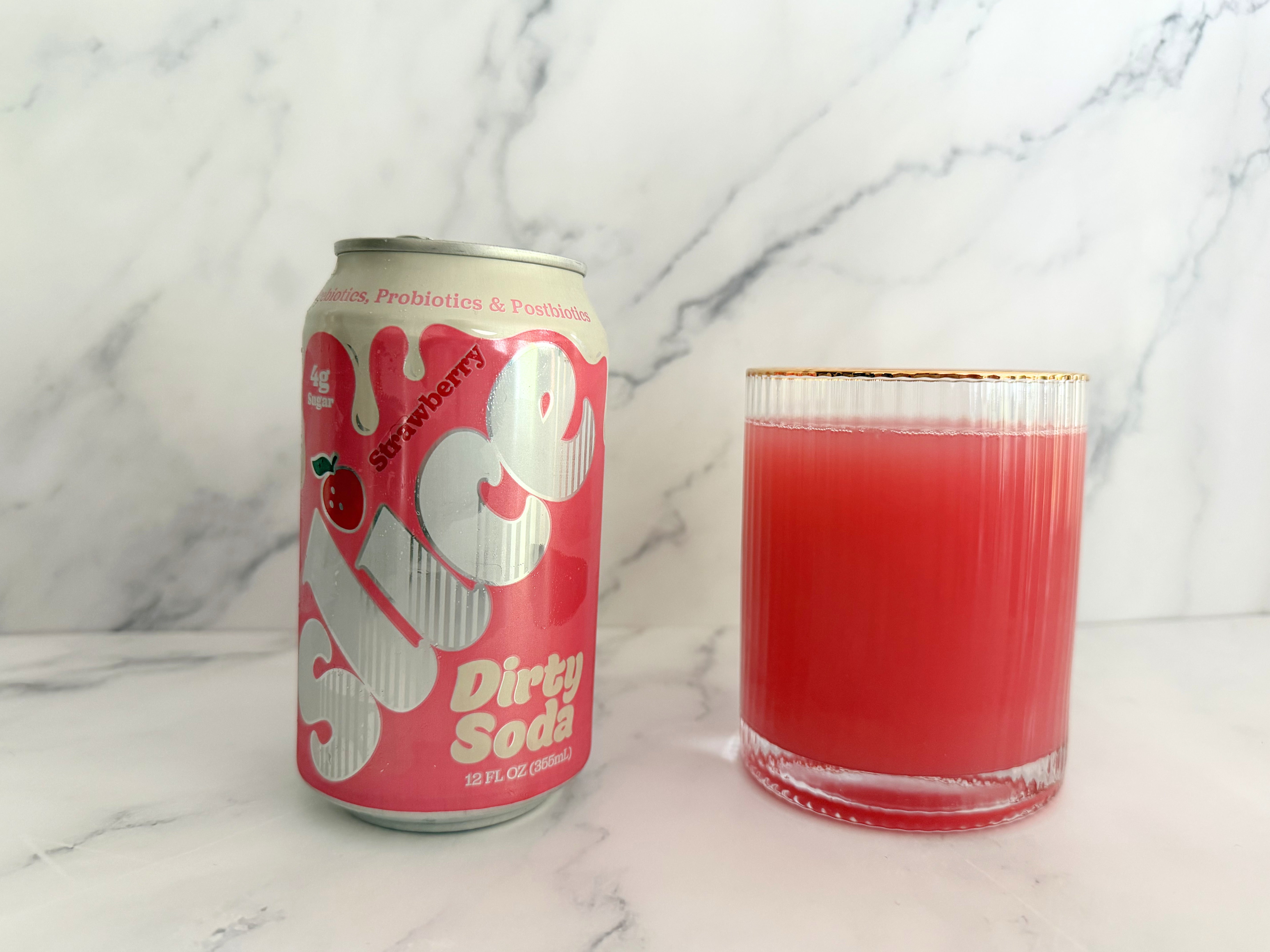 A can of strawberry-flavored Slice Strawberry Dirty Soda next to a glass filled with the pink beverage on a marble surface