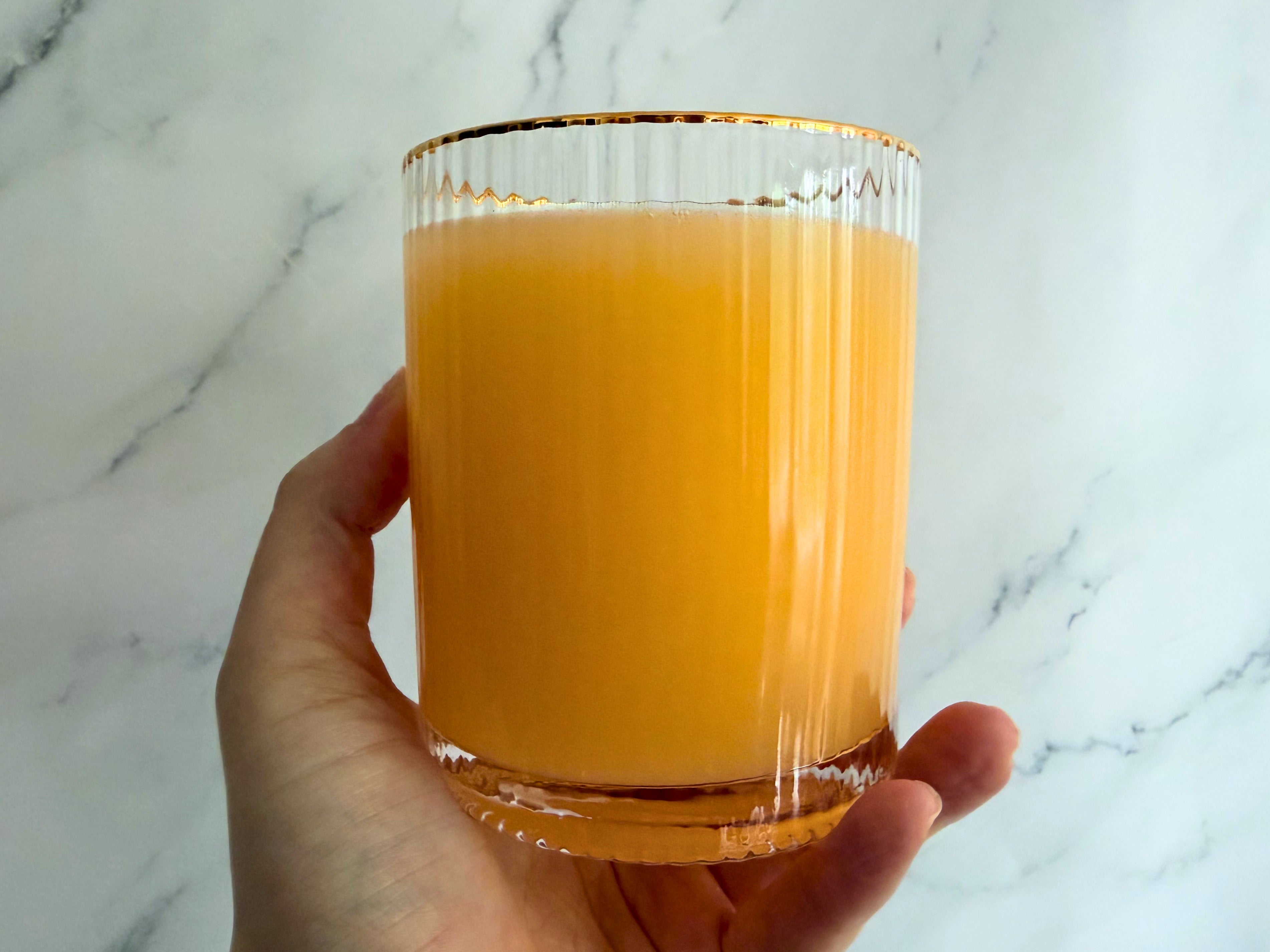 Hand holding a clear glass of Slice Orange Dirty Soda against a marble background