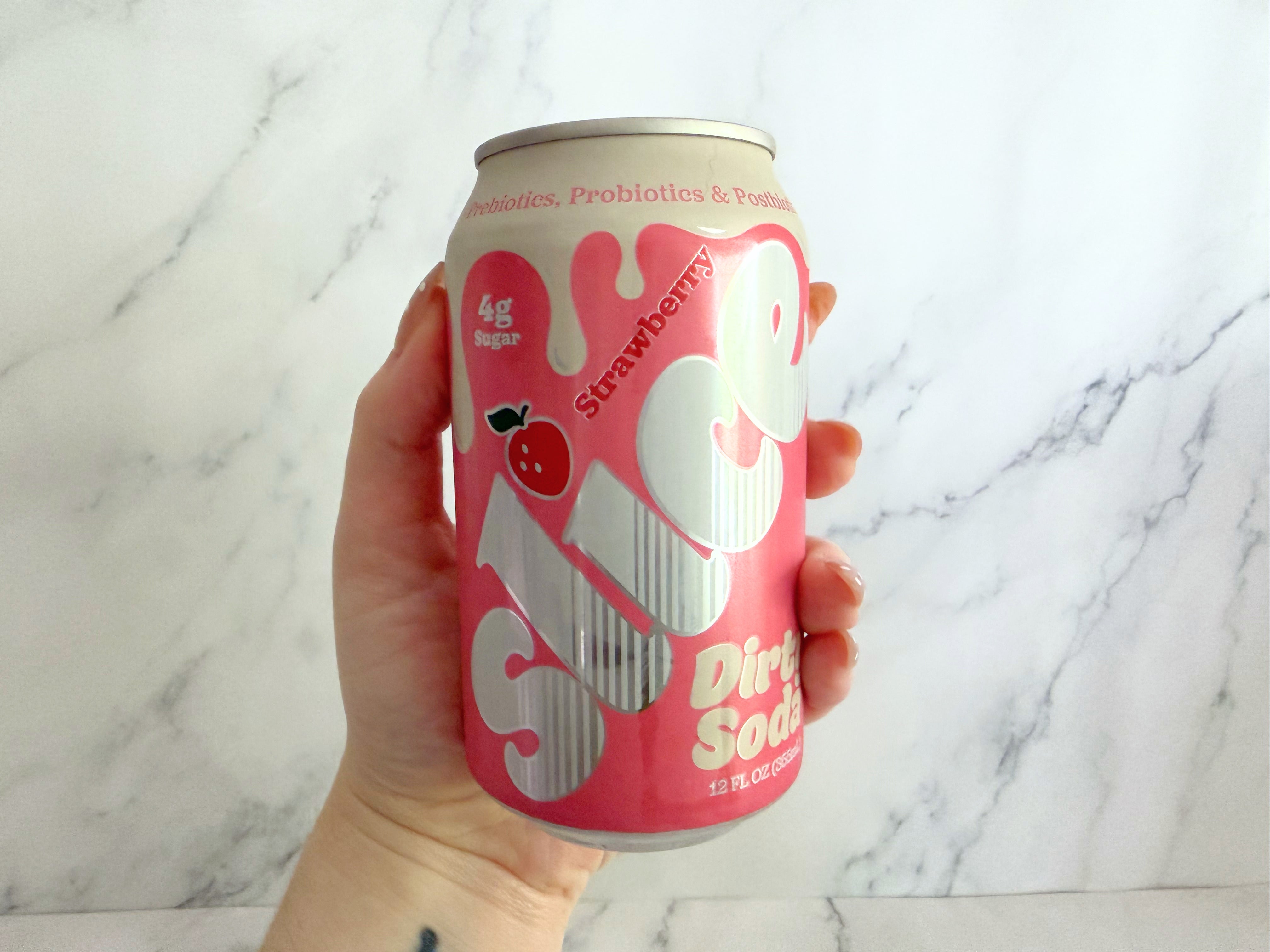 Hand holding a can of Slice strawberry probiotic drink against a marble background