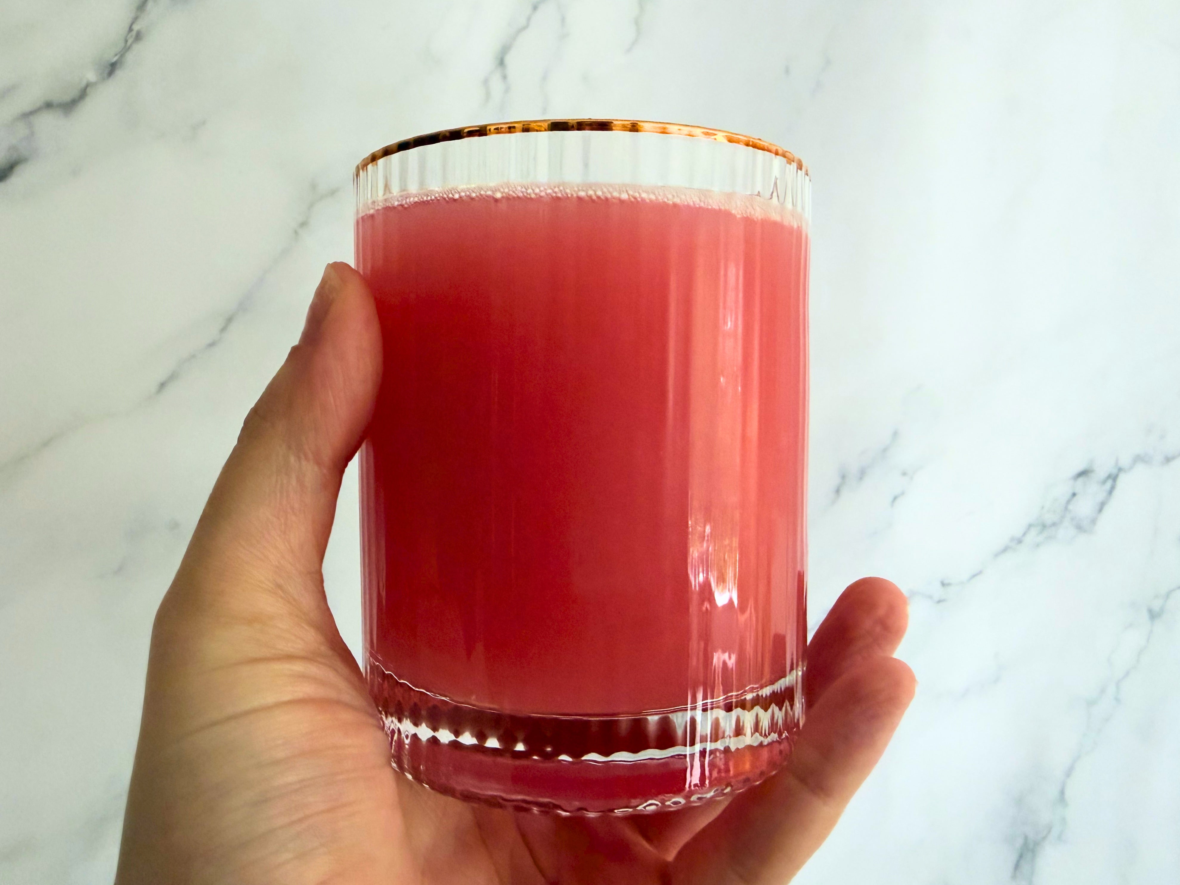 Person holding a glass of pink juice against a marble background