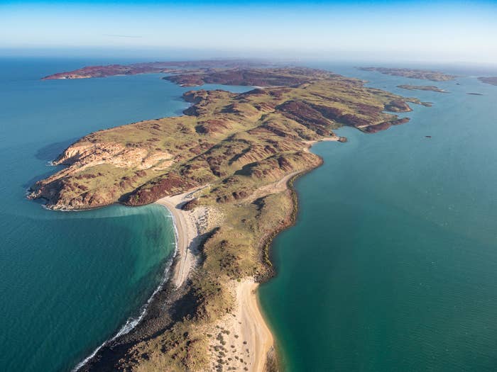 Aerial presumption    of a long, constrictive  land  with grassy terrain and sandy beaches, surrounded by bluish  water  waters