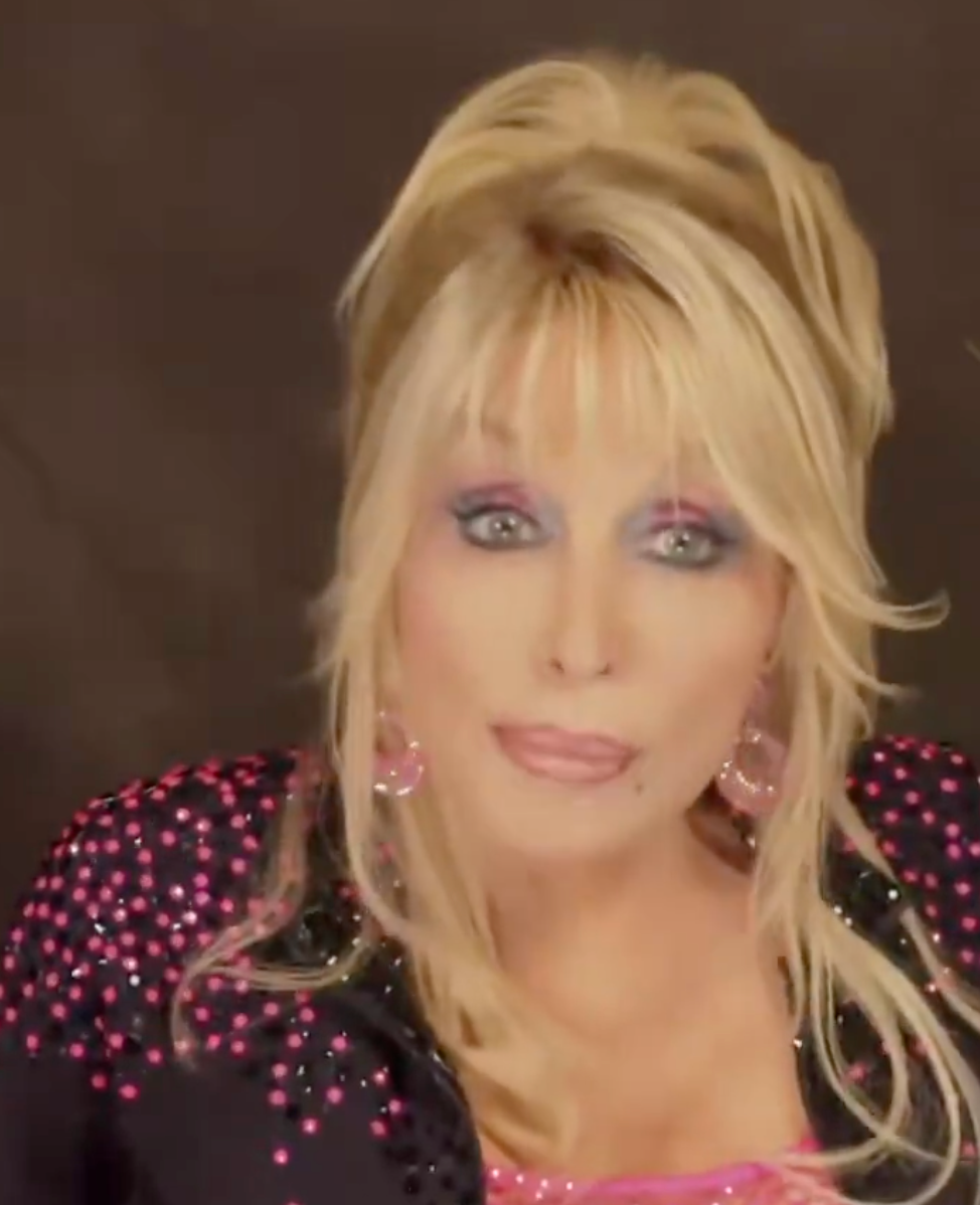 I don’t cognize  who this is, but the idiosyncratic   has styled hair, bold makeup, and is wearing a studded outfit with earrings