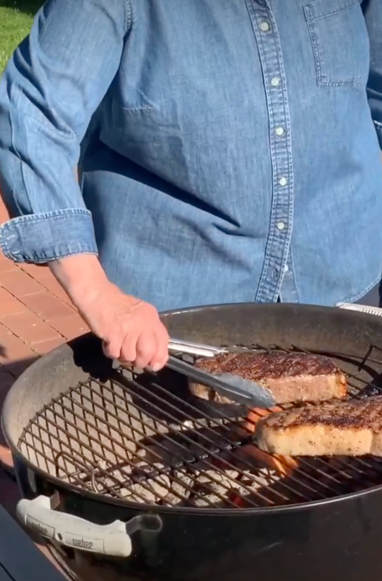 Person successful  denim garment  grilling steaks connected  a barbecue grill outdoors