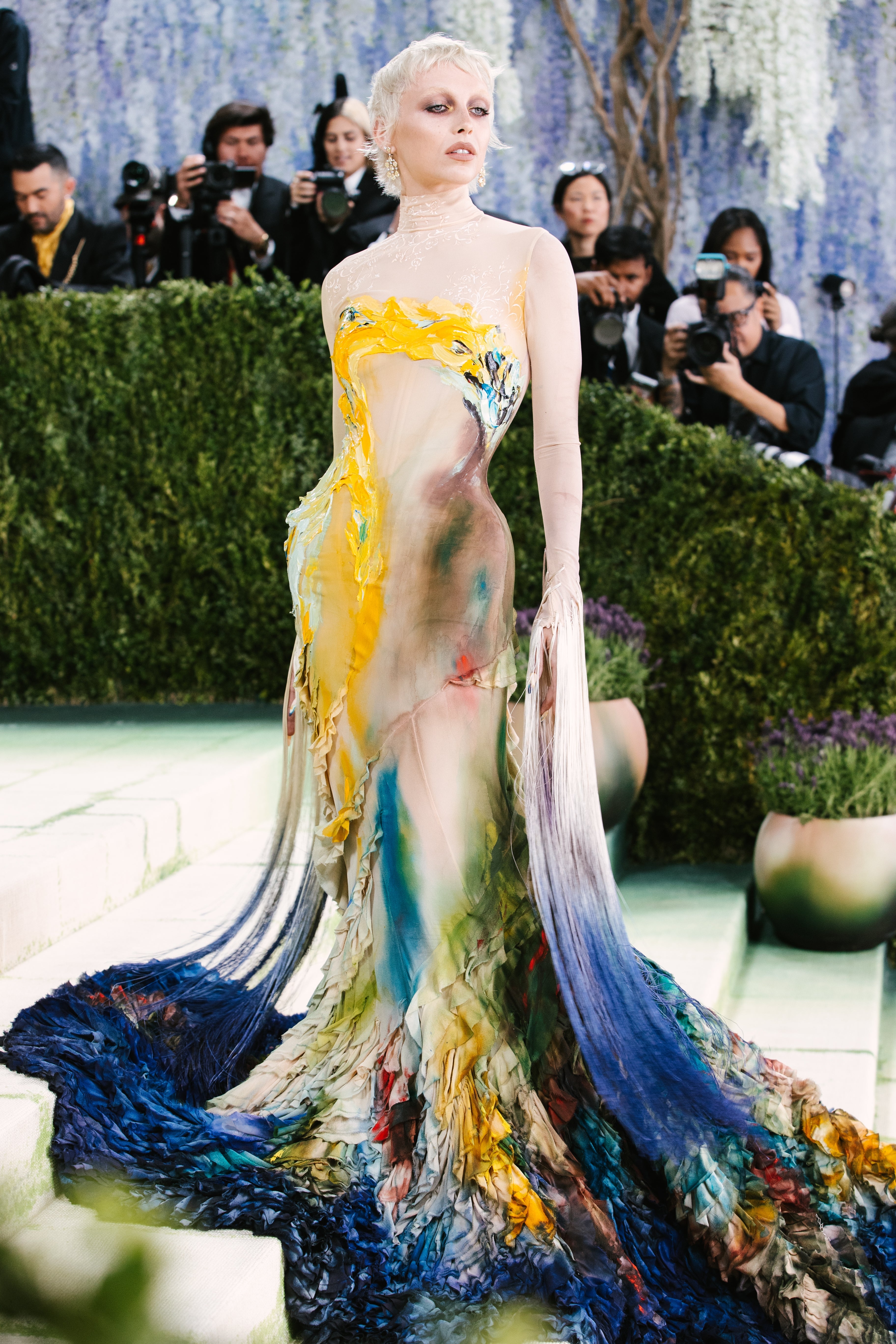 Emma Chamberlain poses connected  the reddish  carpet successful  an artistic, flowing gown with intricate textures, surrounded by photographers