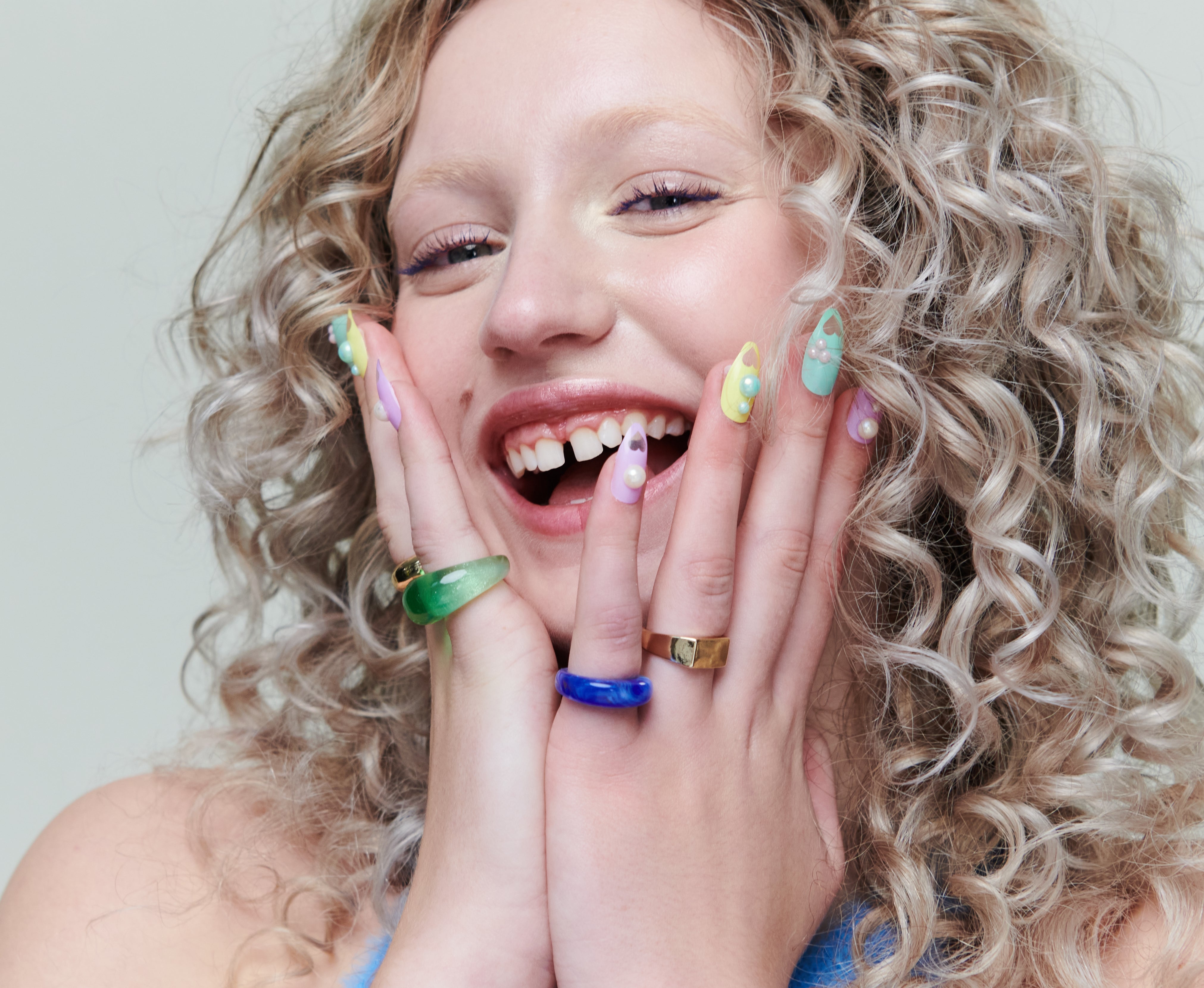 Person with curly hairsbreadth  smiling, hands connected  cheeks, wearing colorful rings and a textured top