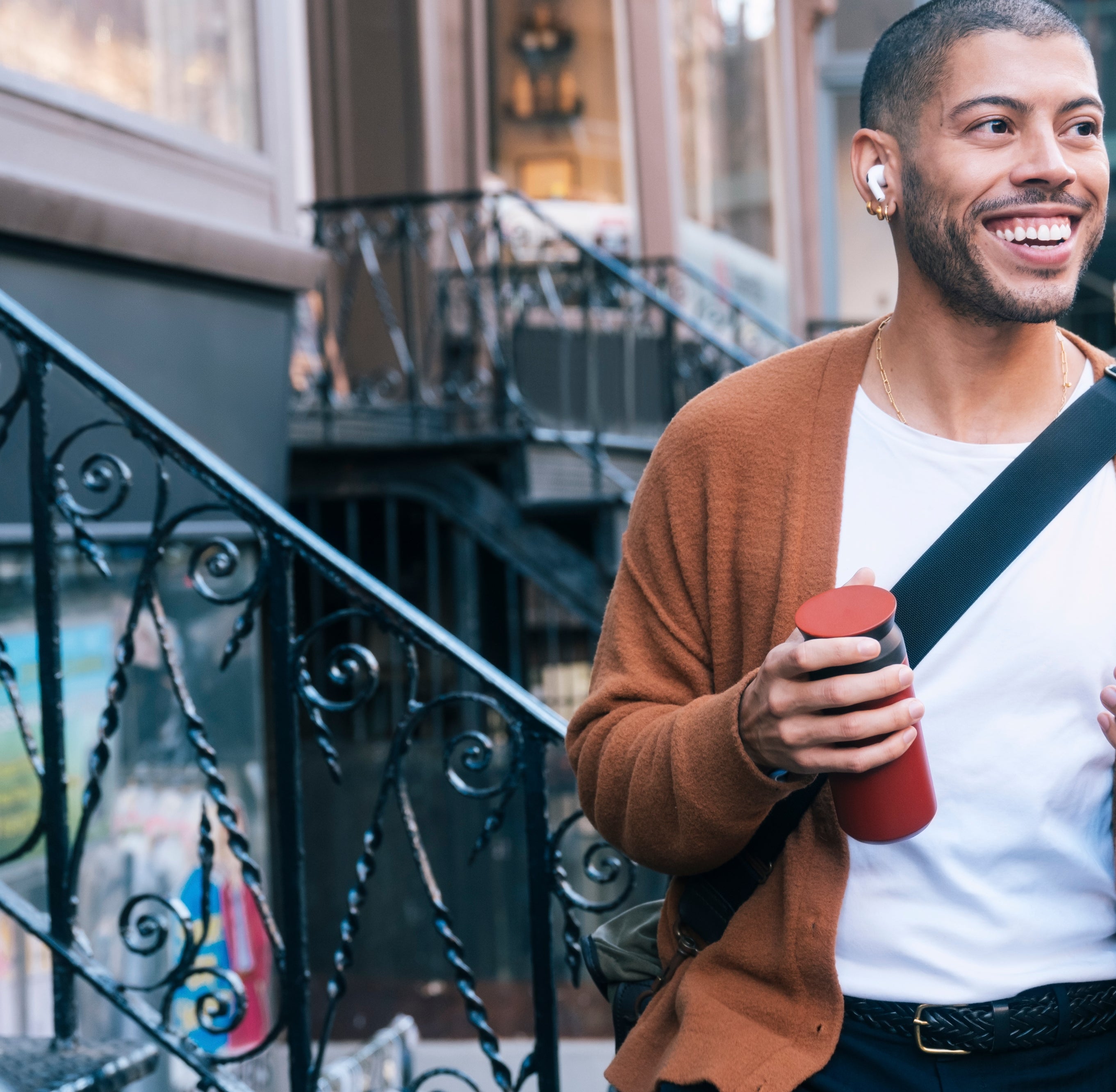 Person smiling portion    walking connected  a metropolis  street, holding a telephone  and a drink, wearing a achromatic  garment  and unfastened  cardigan