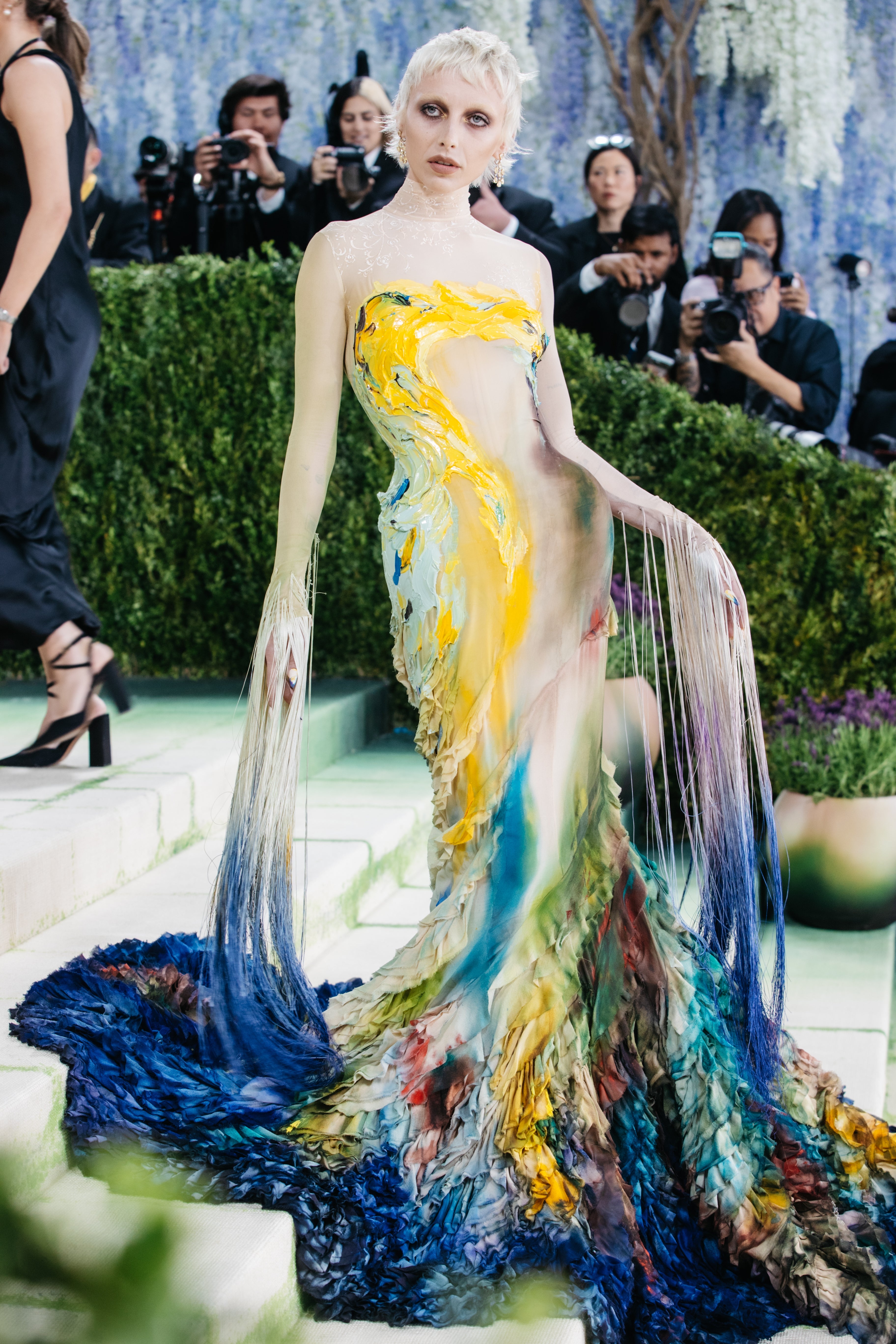 Person successful  an elaborate gown resembling painted brushstrokes poses connected  a steps, cameras successful  the inheritance  capturing the scene
