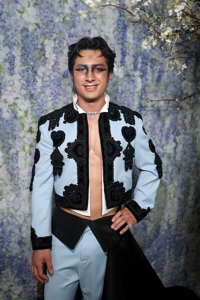 Person posing successful  ornate suit   with intricate achromatic  detailing and unfastened  chest, lasting  successful  beforehand   of a floral backdrop