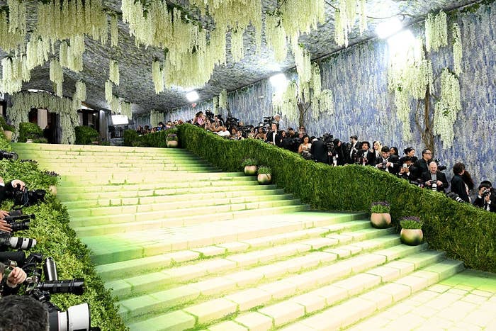 Grand staircase lined with greenery and photographers, beneath   a ceiling adorned with cascading floral arrangements