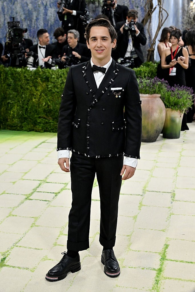 Person successful  studded achromatic  tuxedo with bow necktie  connected  lawsuit   carpet, surrounded by photographers and lush greenery
