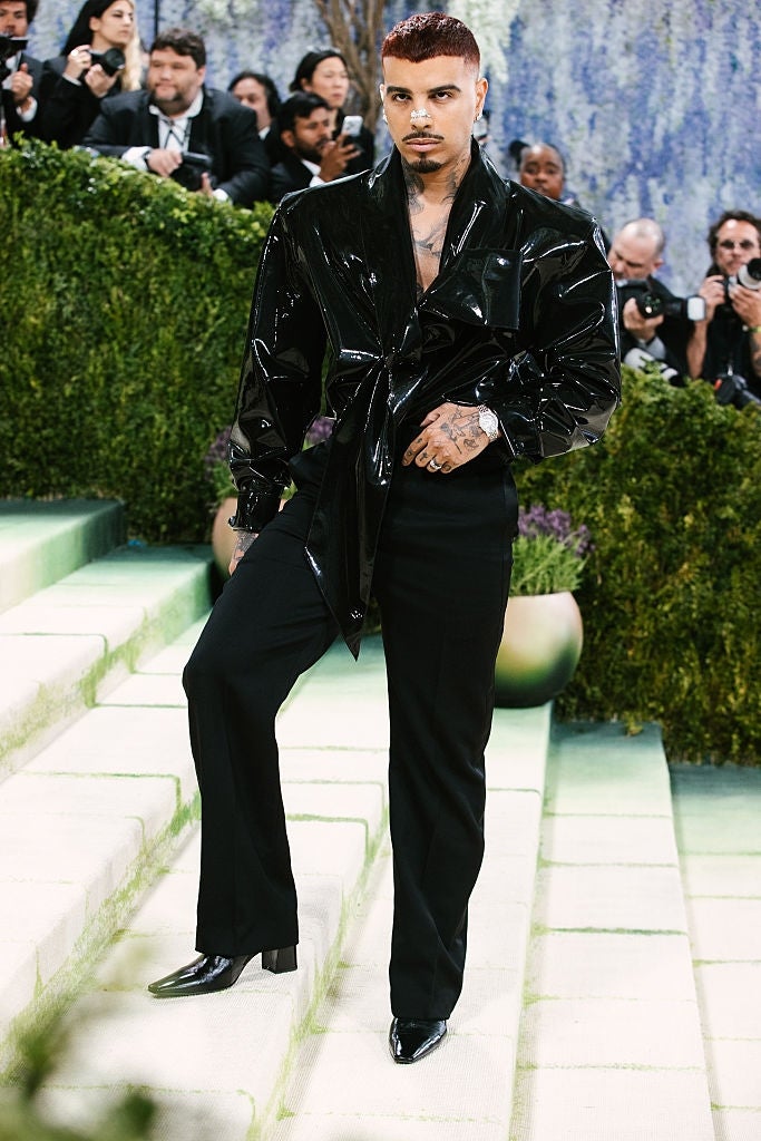 Person successful  a shiny, tailored suit   poses connected  stairs, surrounded by photographers, astatine  a ceremonial  event