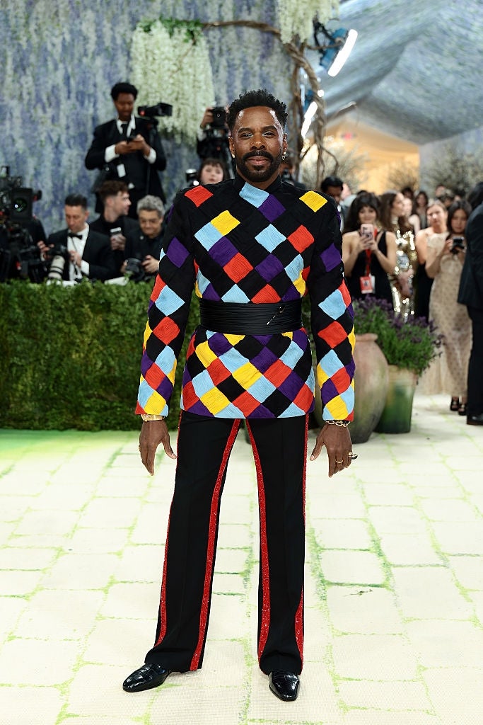 Person successful  a colorful, diamond-patterned suit   poses connected  a manner  lawsuit   carpet. Photographers and attendees successful  the background