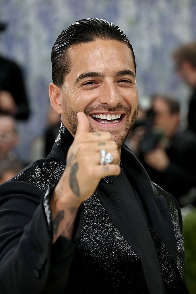 Man smiling and giving a thumbs-up connected  the reddish  carpet, wearing a sparkly, textured suit   jacket
