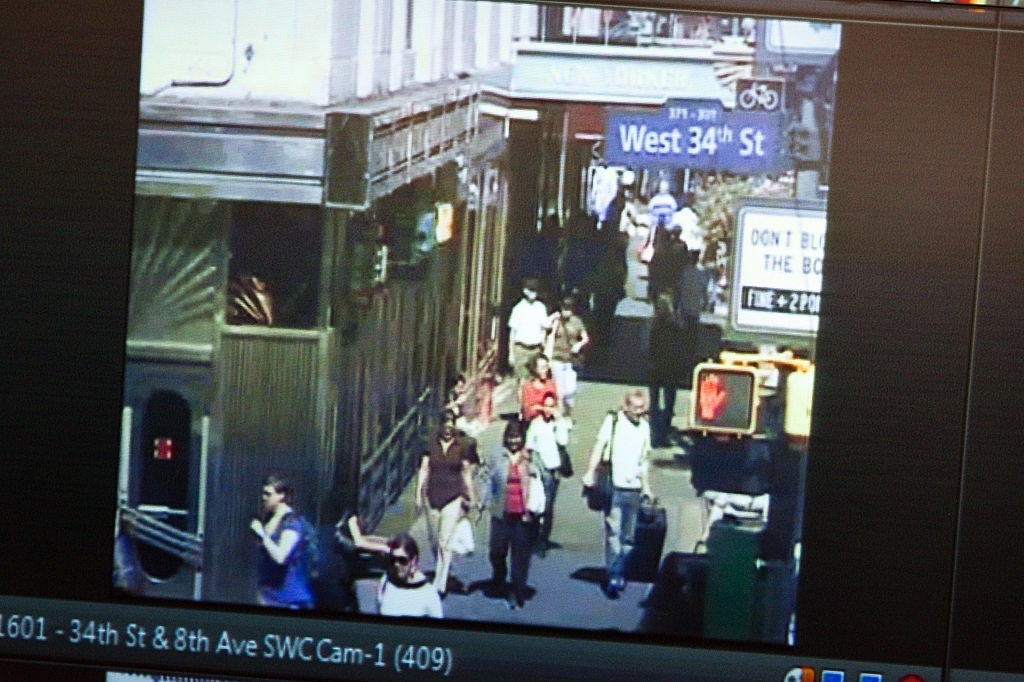Folk som går på et travelt fortau nær West 34th St, New York. Gateskilt og et trafikklys er synlige