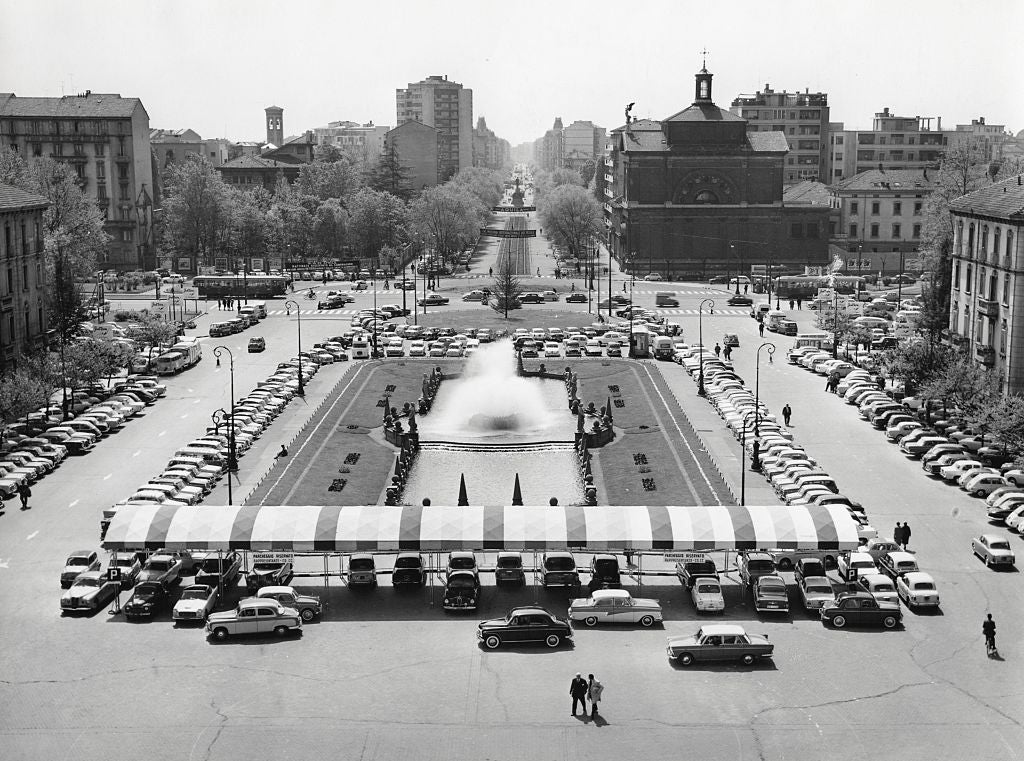 Luftfoto av en overfylt, veteranbilfylt urban scene med en sentral fontene og fjerne bygninger