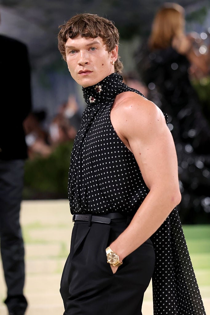 Person successful  a sleeveless, high-neck polka dot apical  with a agelong  scarf detail, posing confidently with hands successful  pockets connected  a ceremonial  lawsuit   carpet