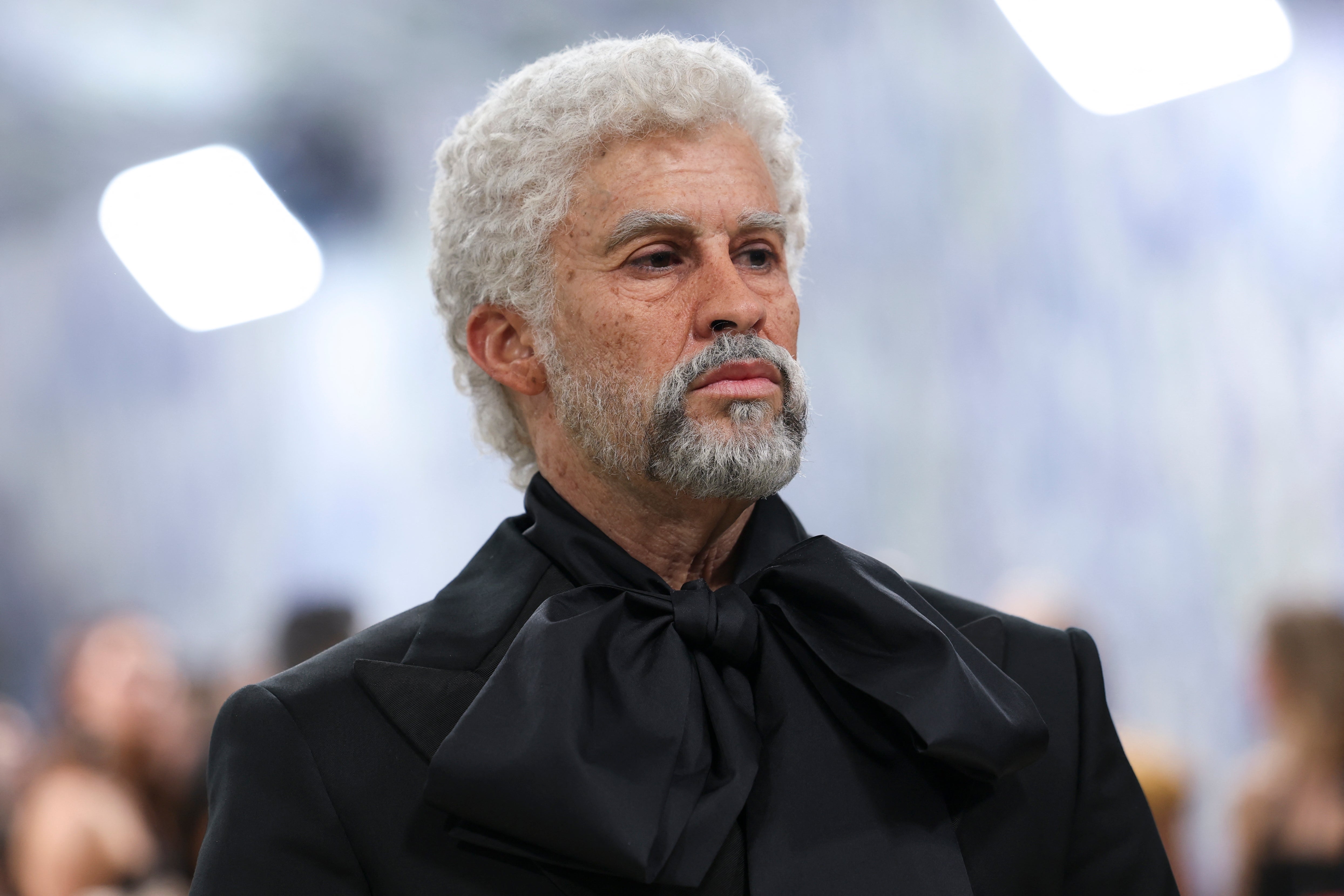 An older idiosyncratic  with curly hairsbreadth  and a beard wearing a ceremonial  suit   with a ample  bow tie. The inheritance  appears blurred