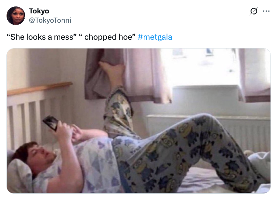 Orang yang sedang bersantai di tempat tidur, mengenakan piyama bermotif, menggunakan ponsel, dengan teks lucu yang merujuk pada Met Gala