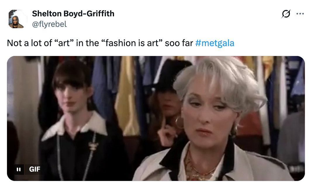 Seorang wanita dengan rambut pendek dan jas putih terlihat tidak terkesan, dengan wanita lain di latar belakang. Tweet tersebut mengomentari pilihan fesyen Met Gala