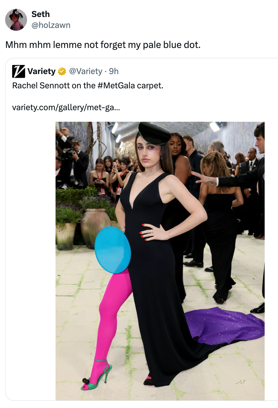 Rachel Sennott di Met Gala dalam balutan gaun hitam dengan celana ketat berwarna pink cerah dan topi hitam sambil memegang balon biru