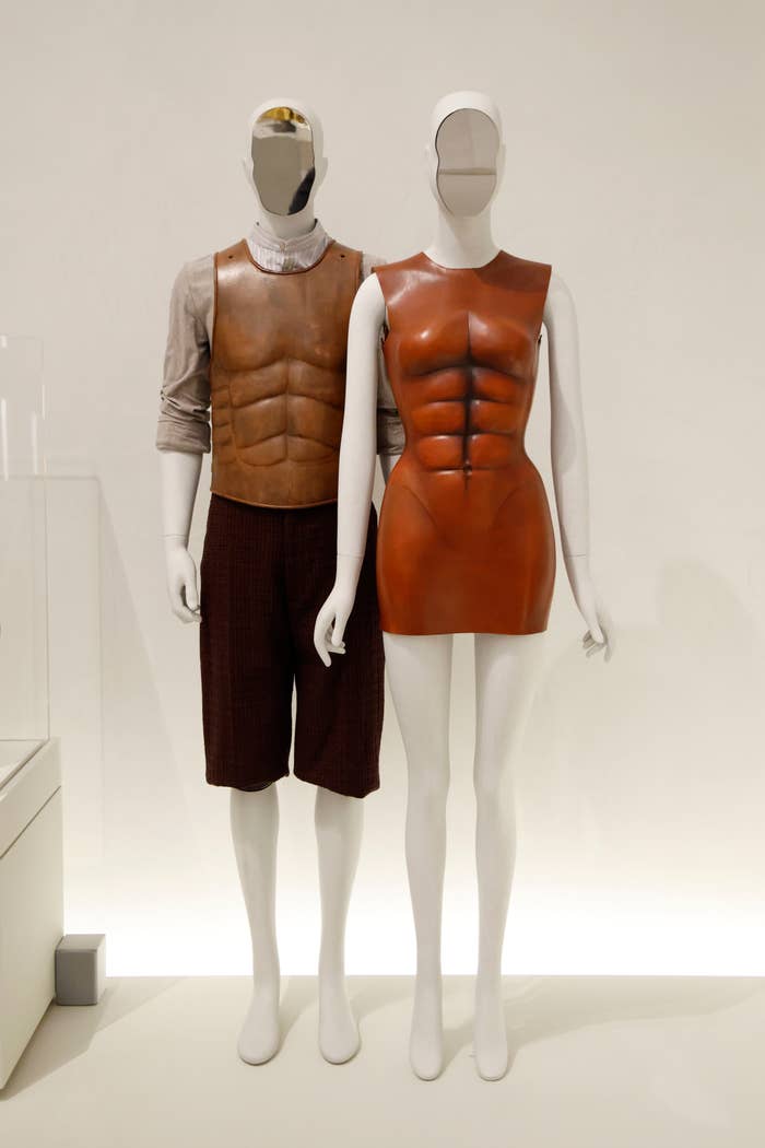Two mannequins showcasing structured, muscle-shaped leather outfits; 1  with a formal  and 1  with a garment  and pants