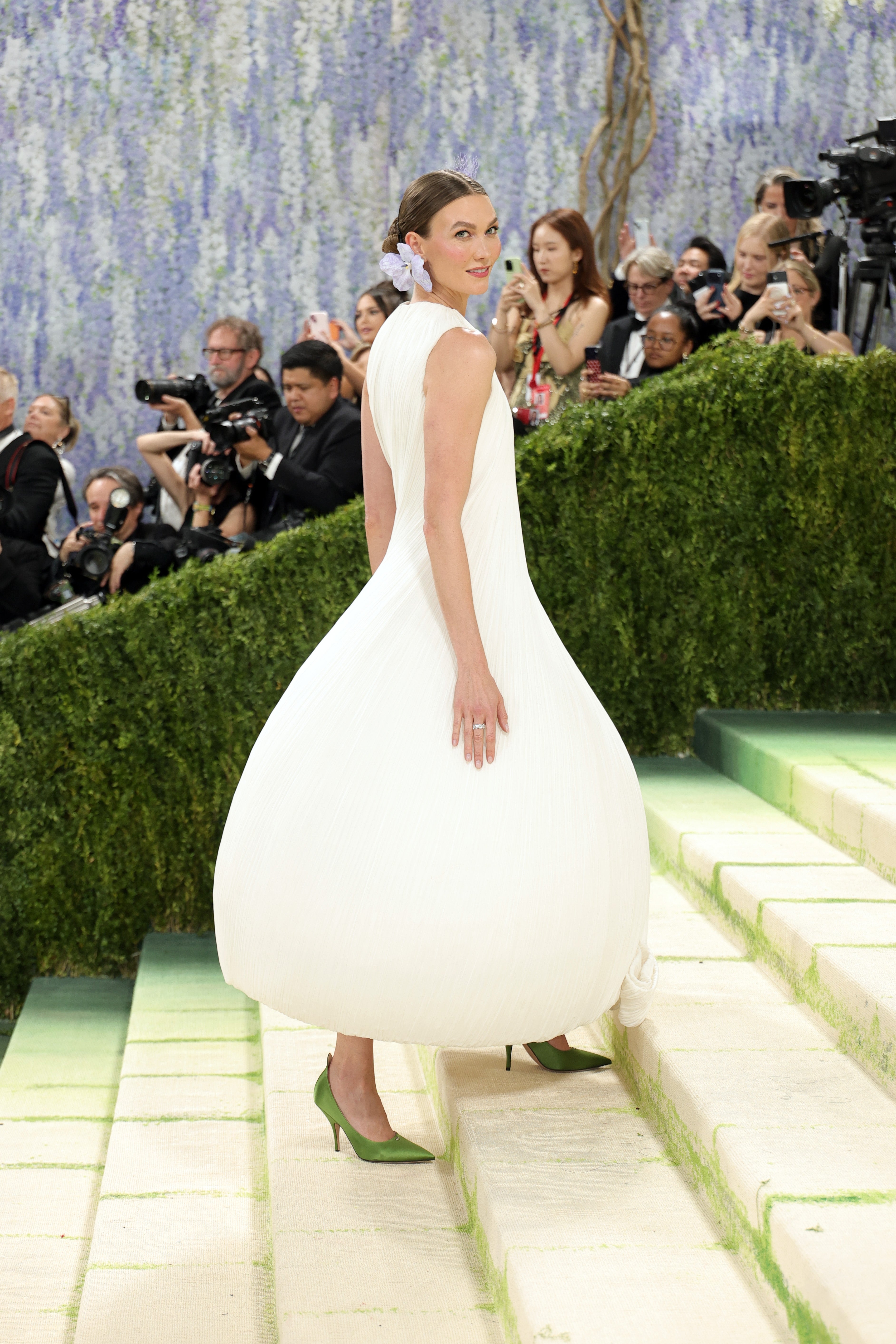 Karlie successful  a sculpted achromatic  gown with greenish  heels, walking up   stairs