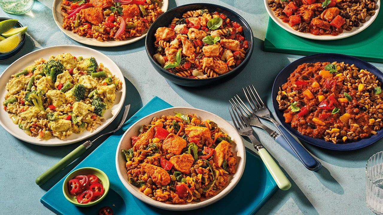 Plates of various dishes with vegetables, rice, and pasta, each with different ingredient combinations, set on a table with utensils