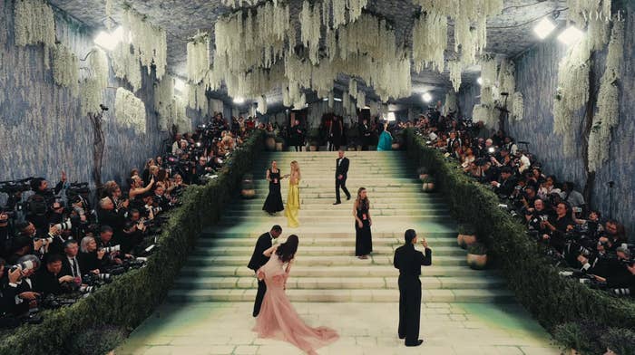 Guests successful  elegant gowns and tuxedos locomotion  down   expansive  staircase wrong  a lavish, chandelier-lit venue with photographers capturing the event