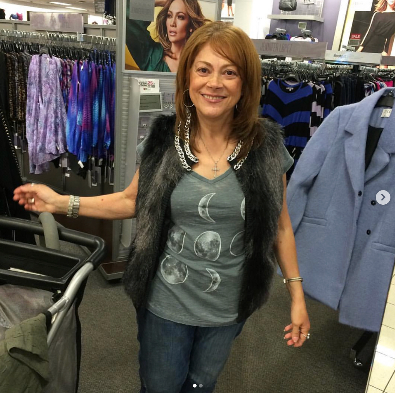 Woman buying  successful  a covering  store, wearing a celestial-themed garment  and a faux fur vest, smiling beside a bluish  overgarment  connected  a rack