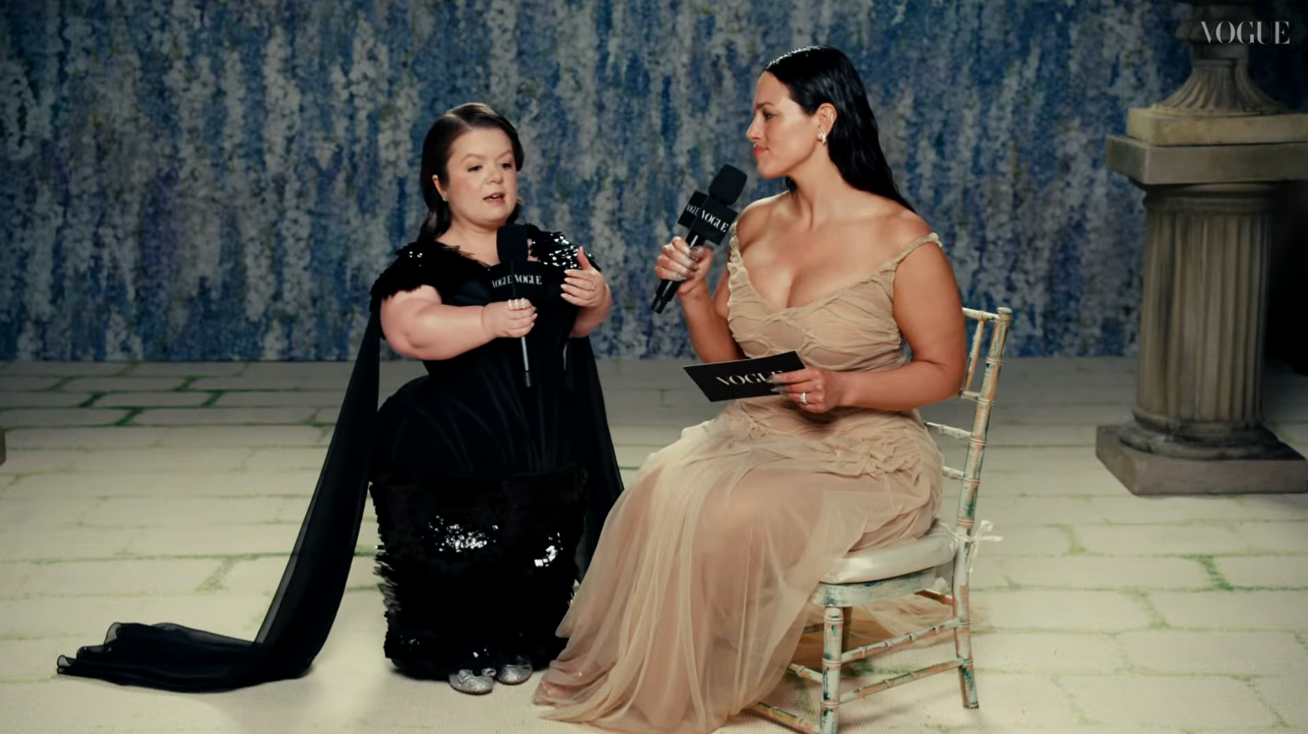 Two women successful  an interrogation  setting; 1  successful  a achromatic  sequined gown, the different   successful  a flowing beige dress, some  holding microphones