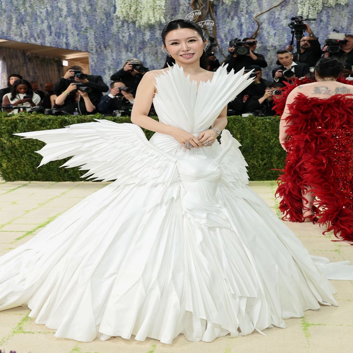 Person in an elaborate white gown with sculptural design on a formal event carpet, surrounded by photographers
