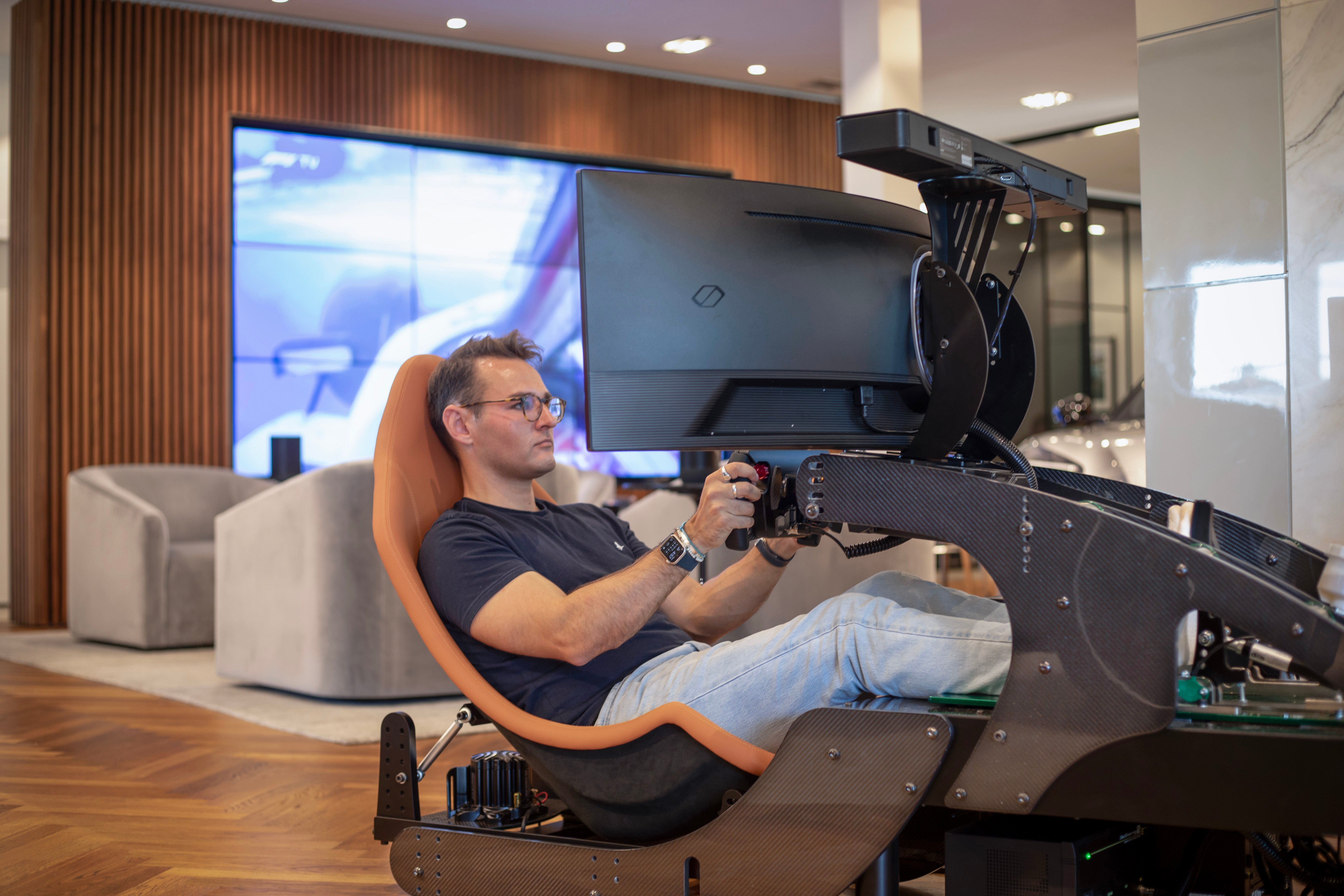 Person seated in a racing simulator setup, holding a steering wheel and focusing on the screen ahead