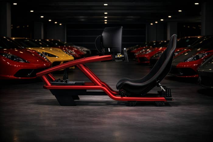 Racing simulator setup in a garage with sports cars lined up in the background, featuring a sleek seat and monitor mount