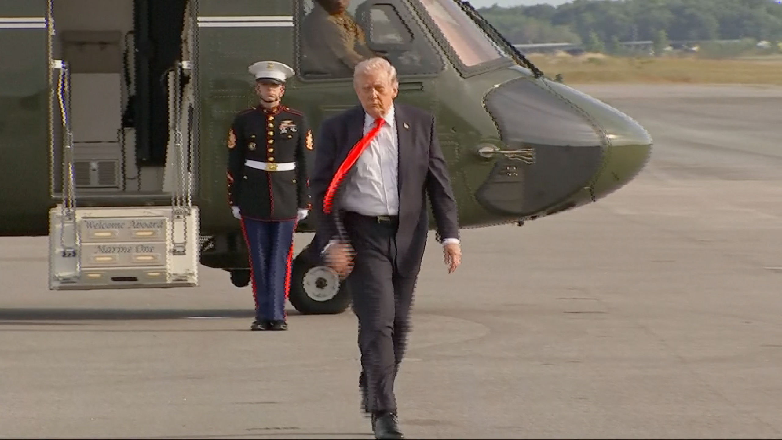 Person successful  suit   with a reddish  necktie  walks distant  from a chopper  connected  a runway, Marine stands successful  the background