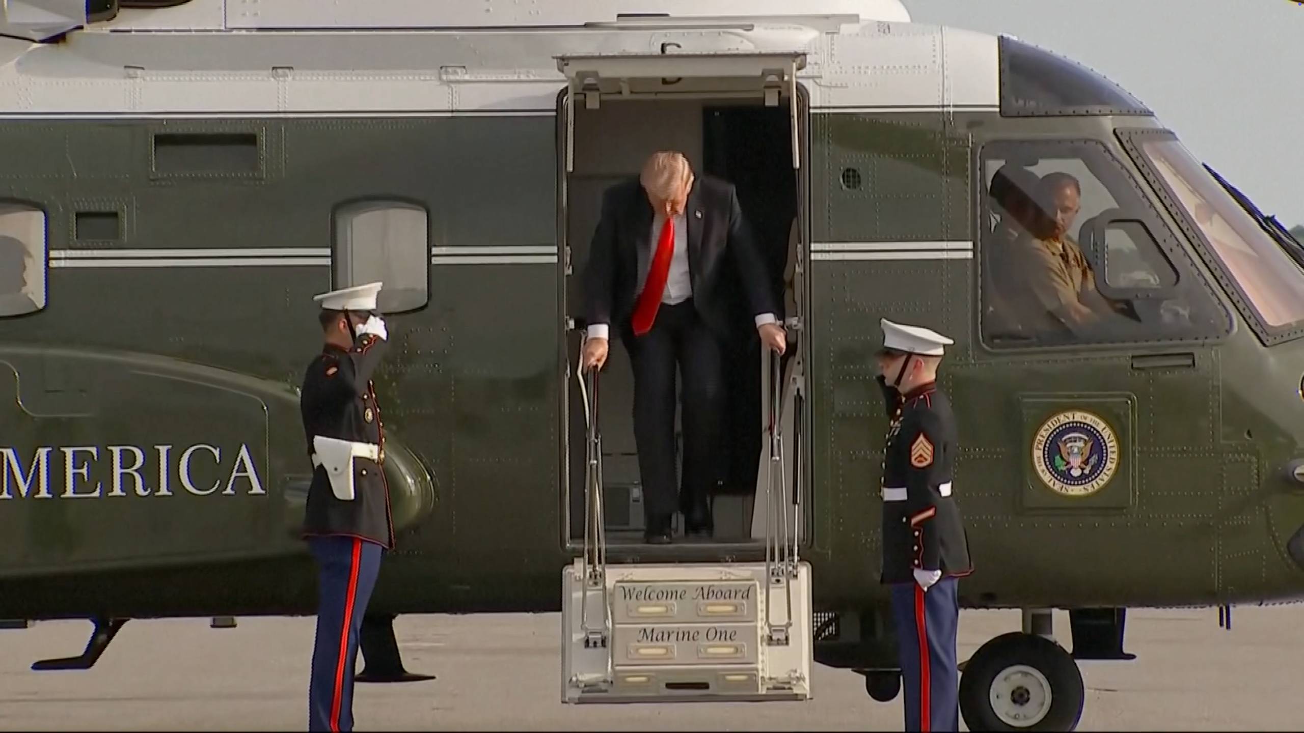 Individual exiting a helicopter, greeted by 2  uniformed subject   personnel. Helicopter doorway  displays "United States of America" and the statesmanlike  seal
